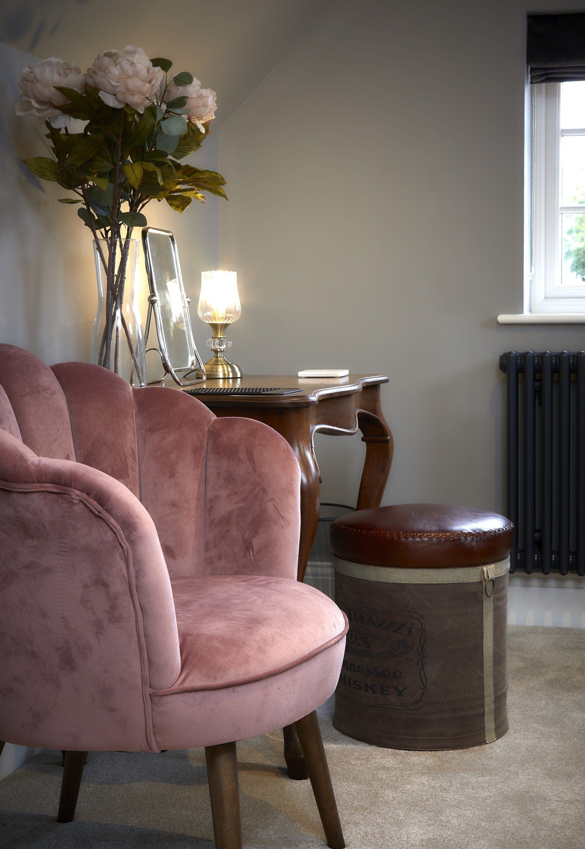 A pink chair is sitting next to a table with a vase of flowers on it.