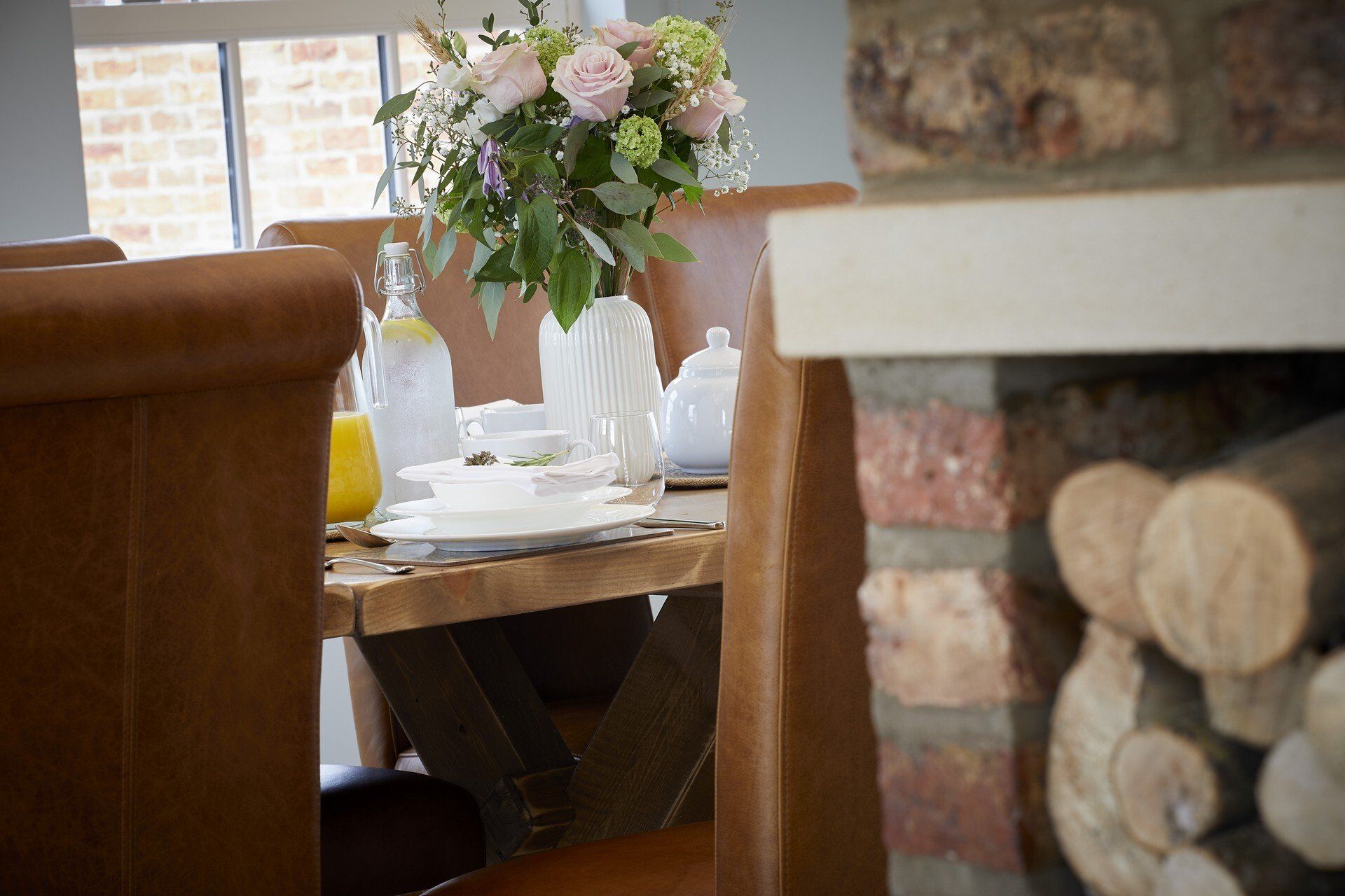 A dining room table with a vase of flowers on it and a fireplace in the background.