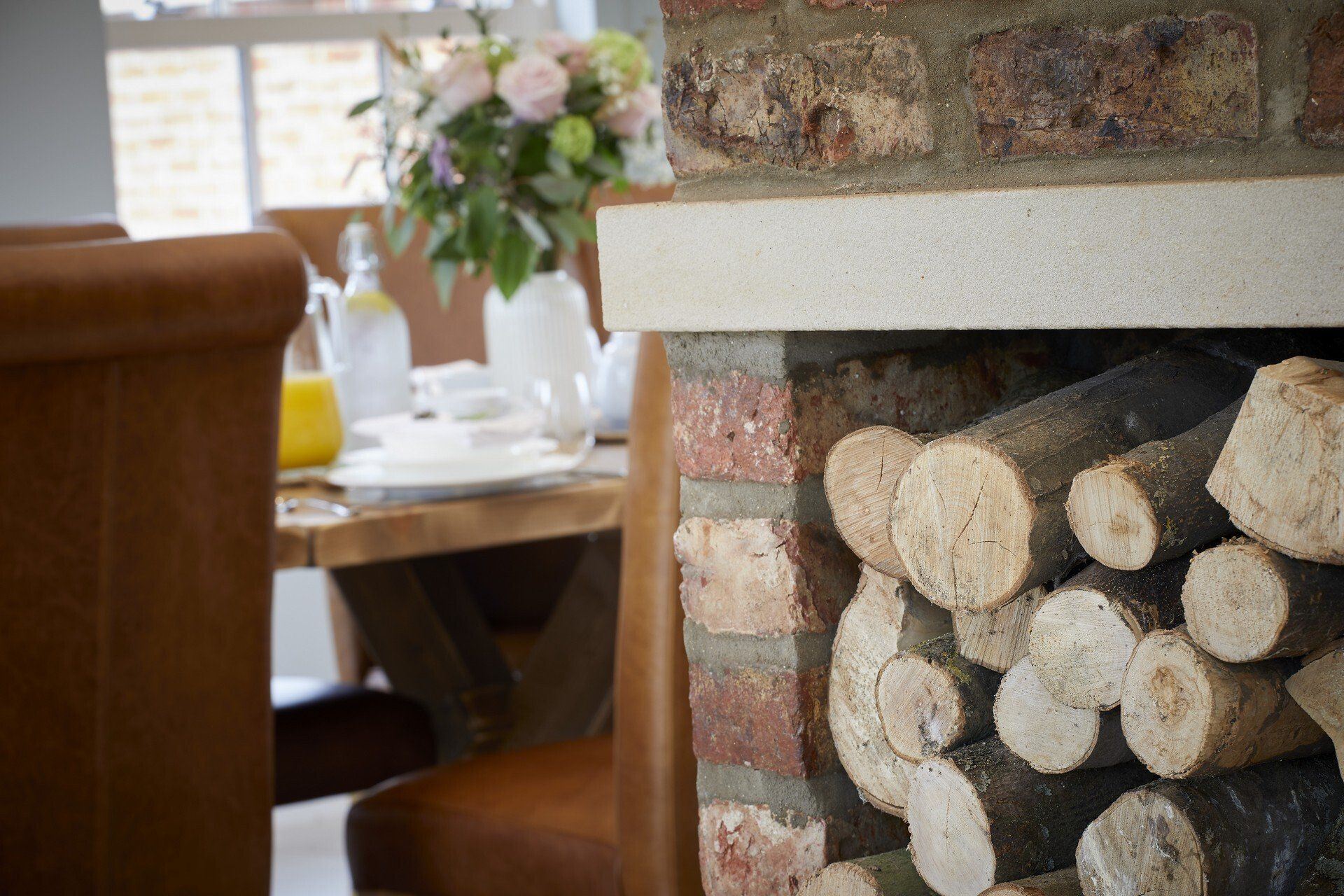 A fireplace filled with logs in a dining room with a table and chairs in the background.