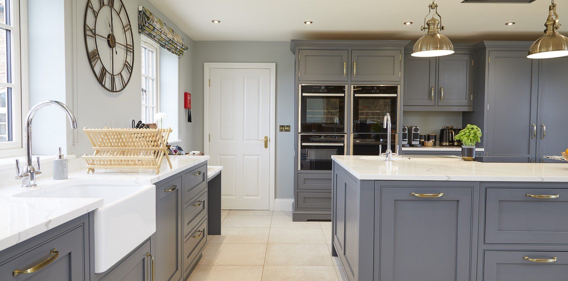 A kitchen with gray cabinets , white counter tops , a sink and a clock on the wall.