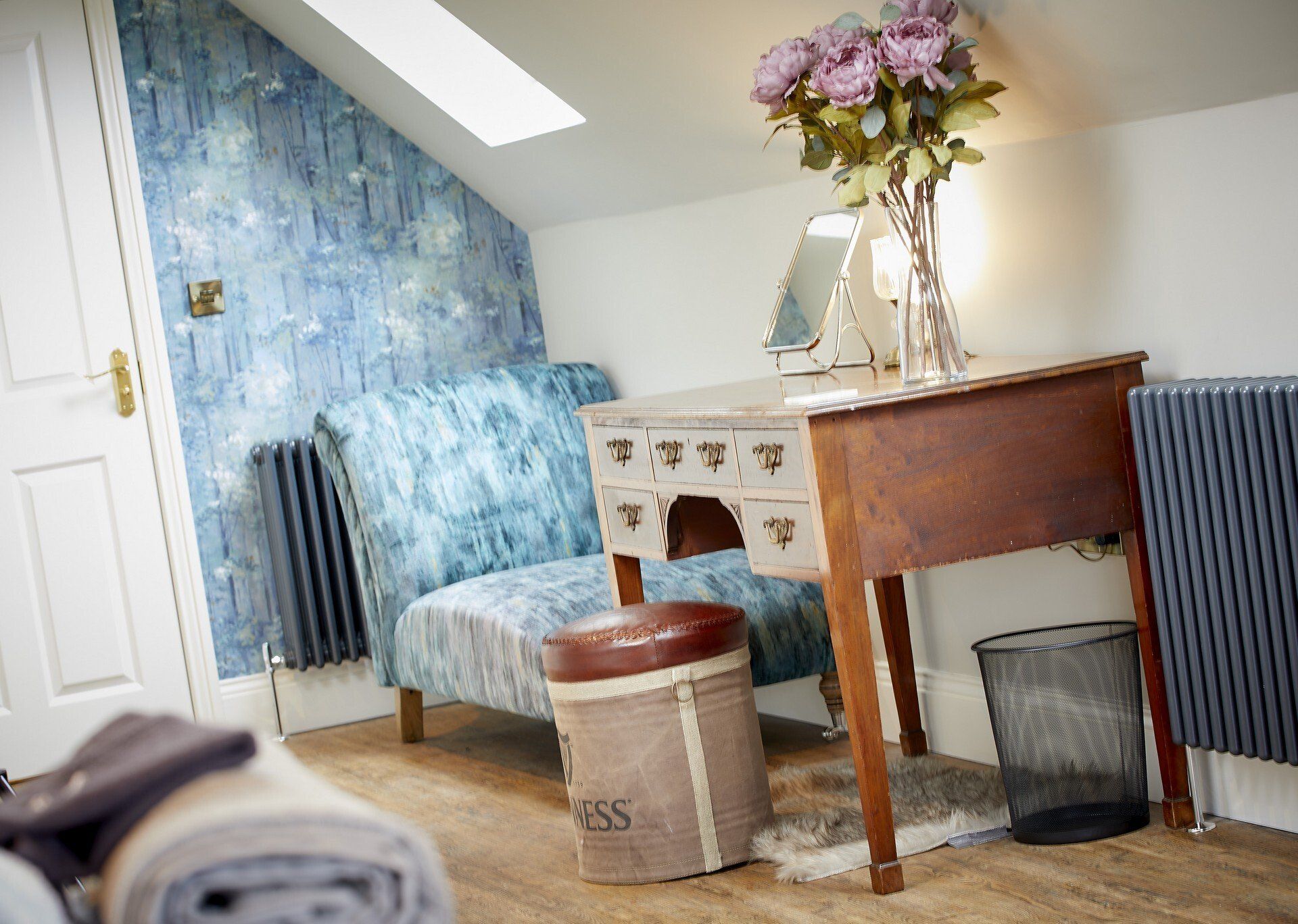 A room with a desk , chair and a vase of flowers.