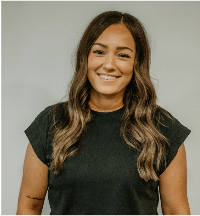 A woman with long hair is wearing a black shirt and smiling.