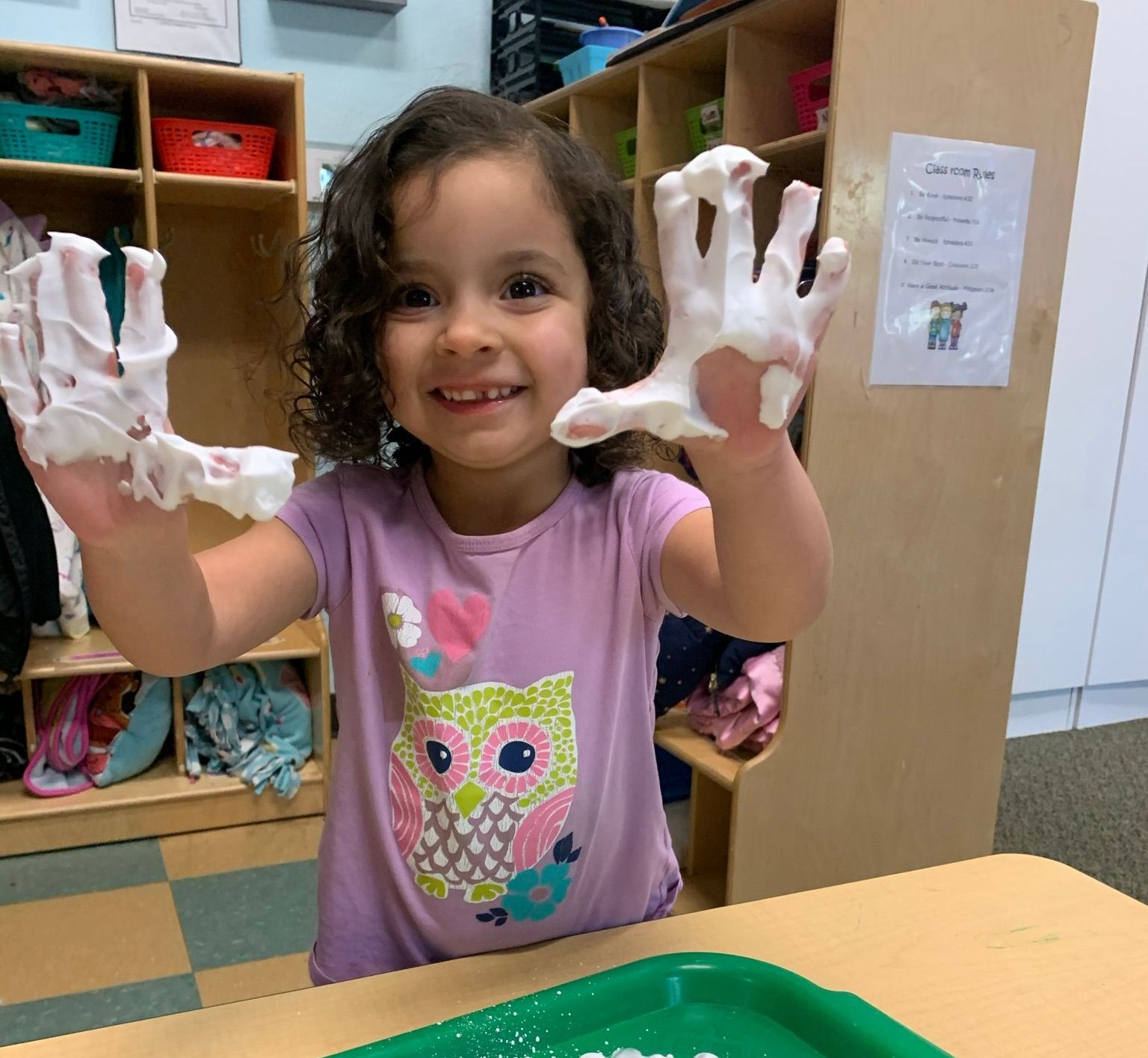 A little girl is playing with shaving cream on her hands.