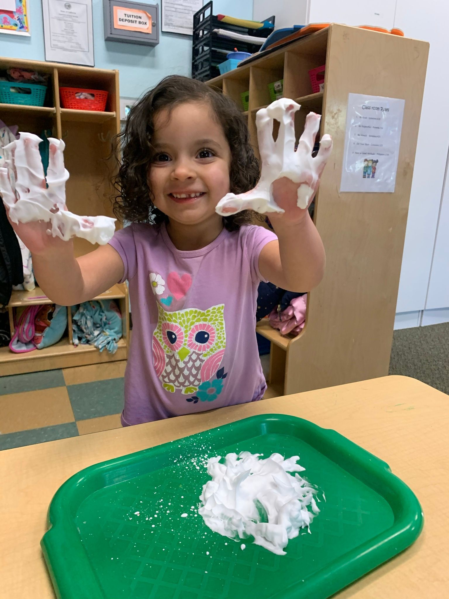 A little girl is playing with shaving cream on her hands.