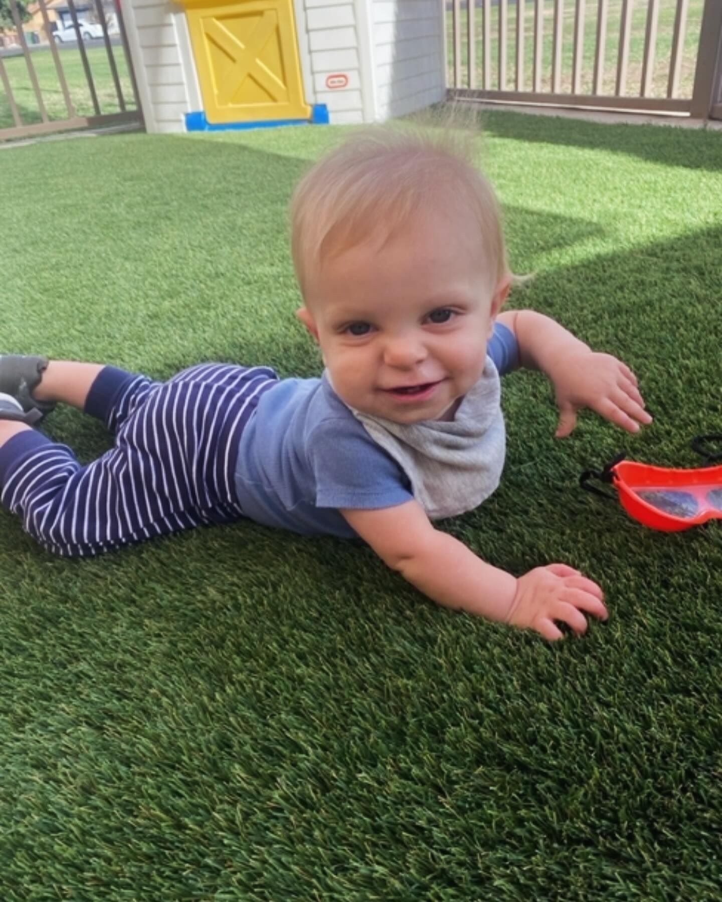 A baby is laying on his stomach on the grass.