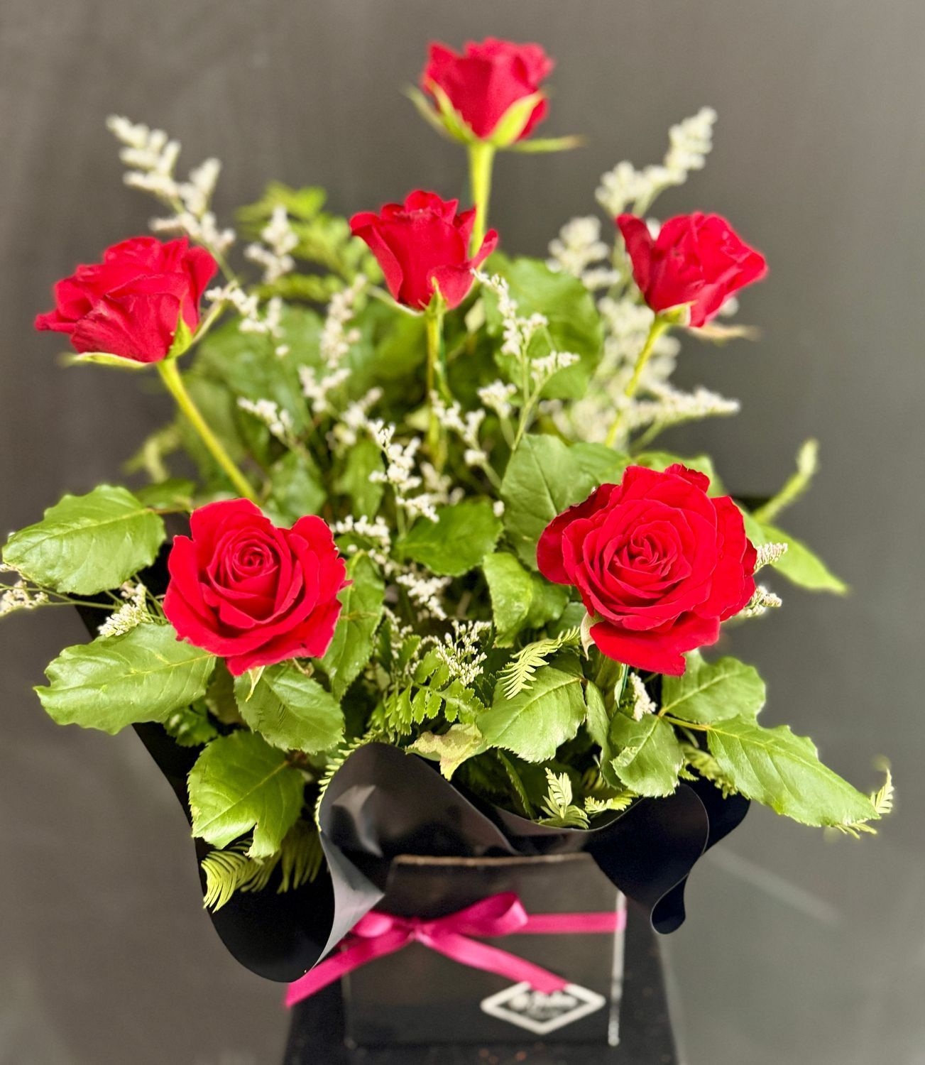 Orange and peach flowers in a white box with black ribbon; green foliage.