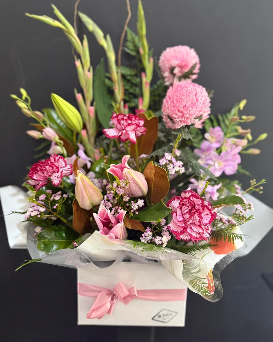Colorful flower arrangement in a white box with gold accents and bow.