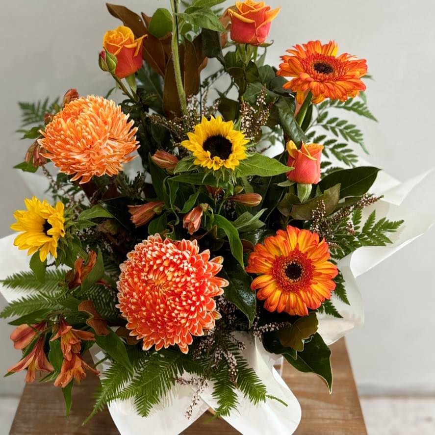 Floral arrangement with orange flowers: roses, gerberas, mums, and sunflowers, wrapped in white paper — J'adore Flowers & Gifts Cairns in Earlville, QLD