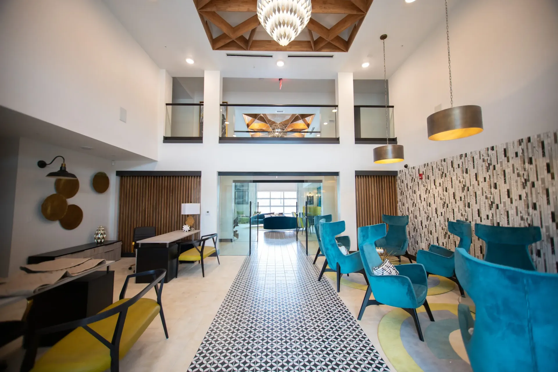 Bright apartment community lobby with teal chairs, glass doors, and a second-floor balcony.