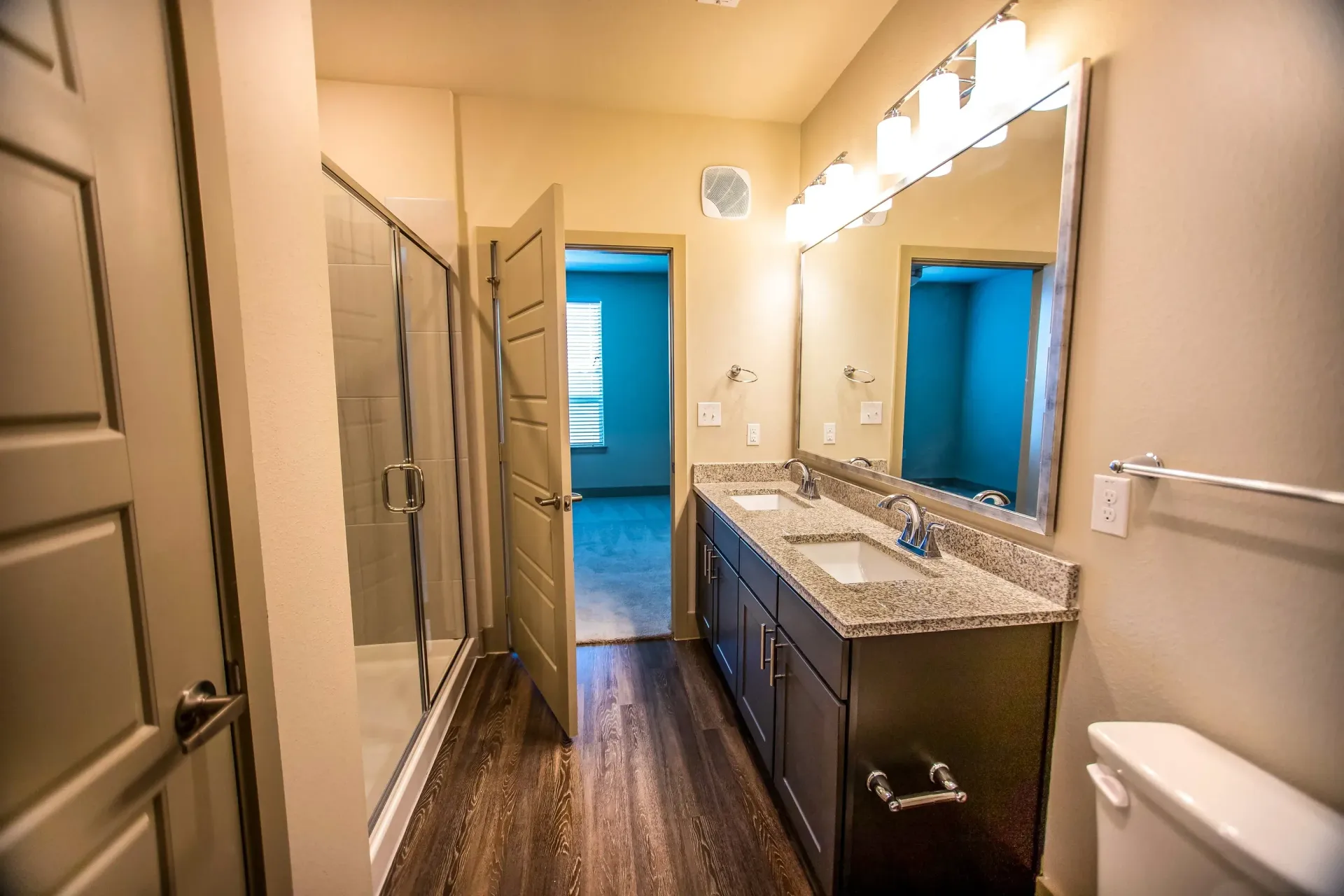 Bathroom with a double-sink vanity, granite countertop, and glass-enclosed shower.