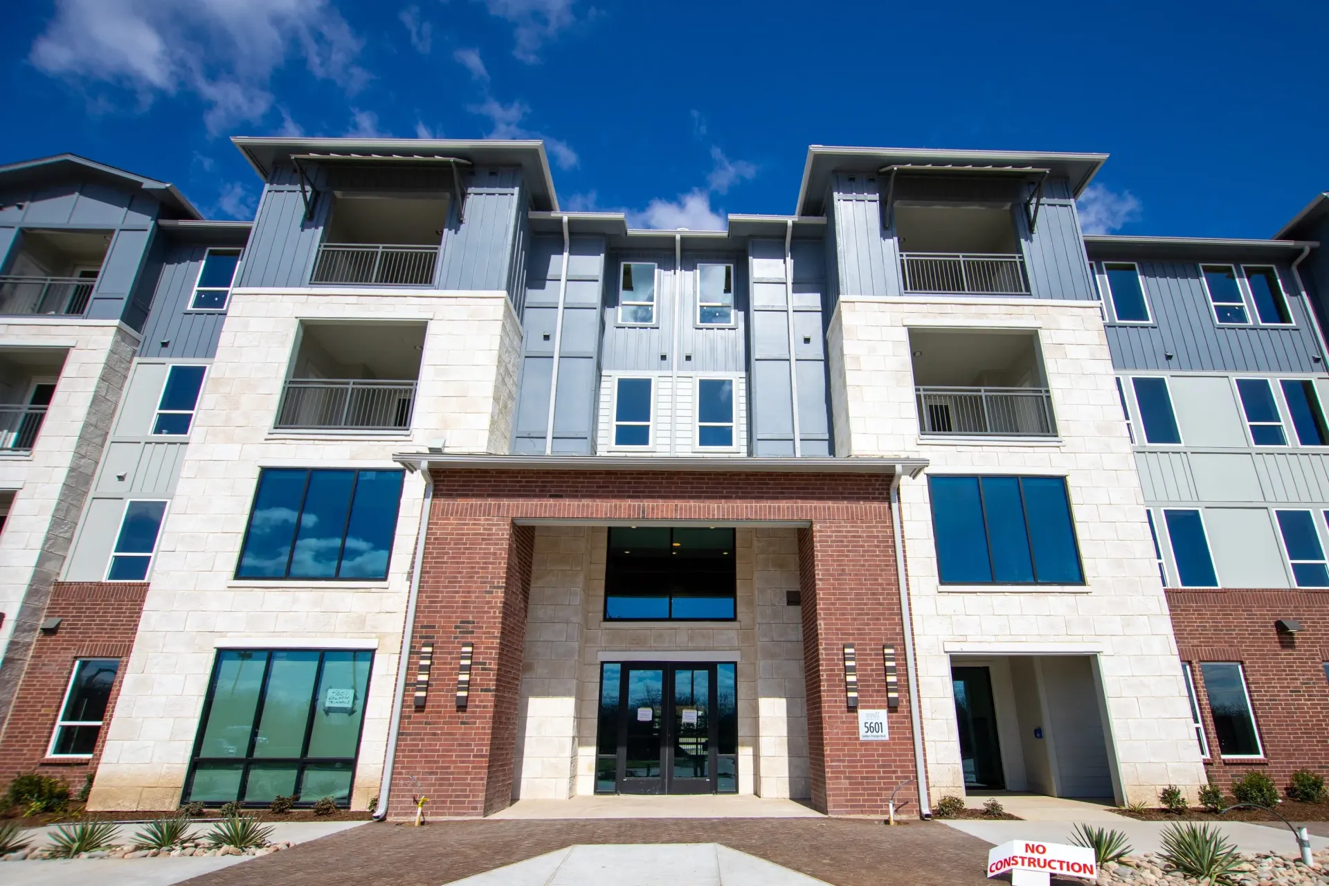 Exterior view of a modern apartment building with brick and stone facade and a central entryway.