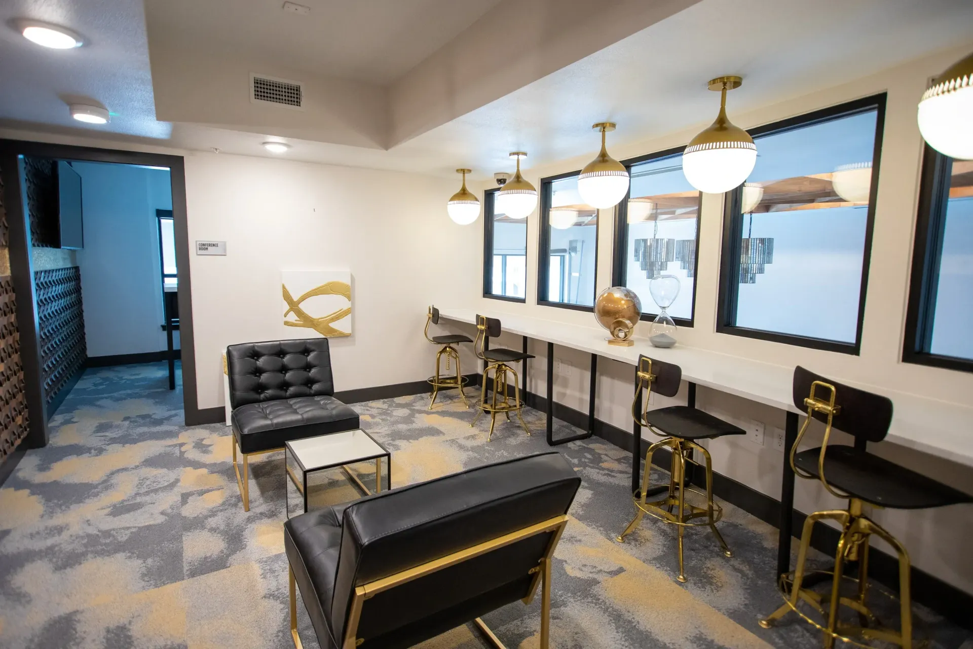 Interior community lounge with black leather seating, gold accents, and a windowed bar counter.