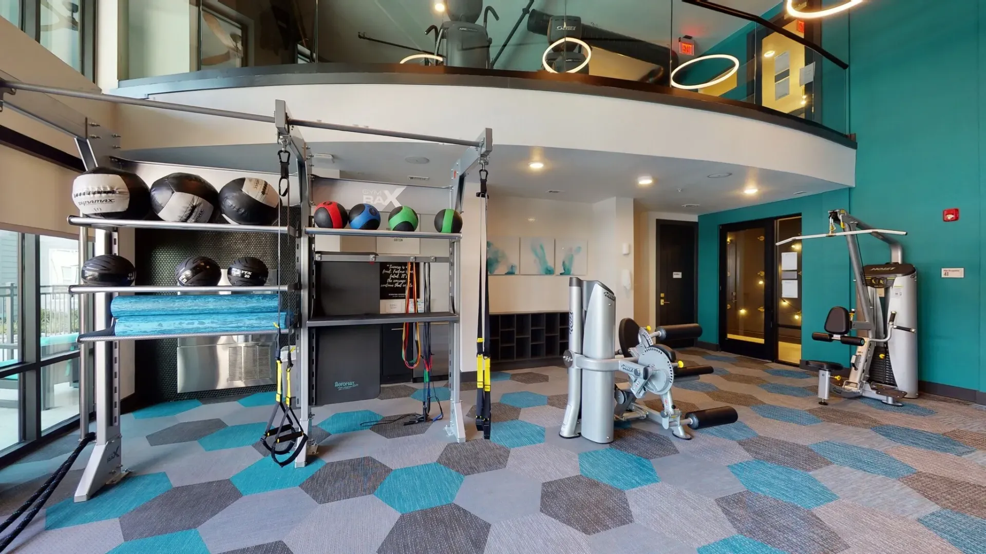 Indoor community gym with weight racks, medicine balls, mats, and resistance training gear.