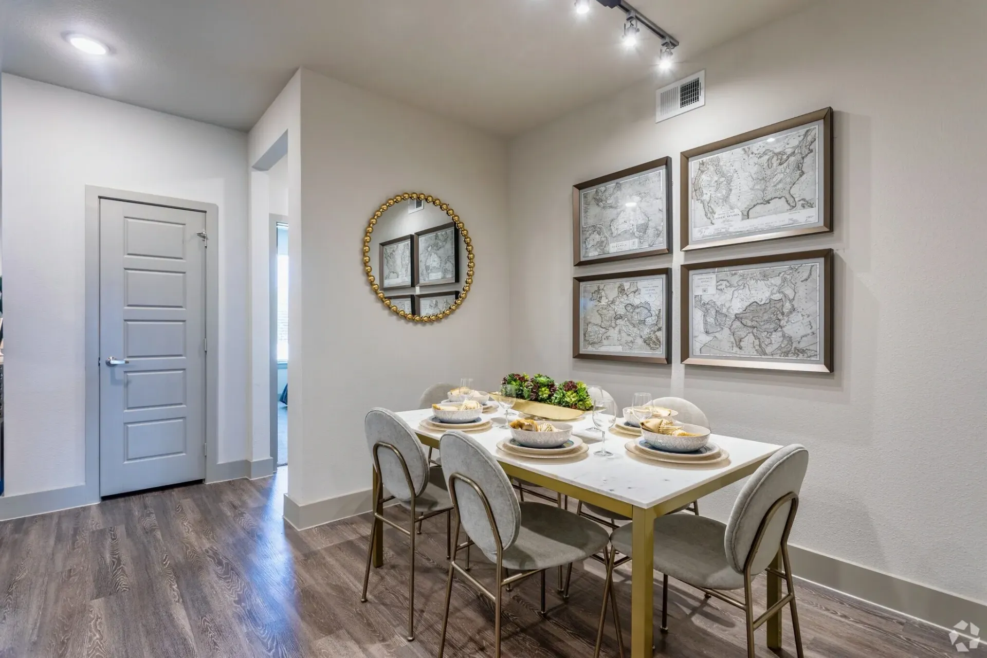 Dining nook in an apartment with a table, six upholstered chairs, wall maps, and a round mirror.