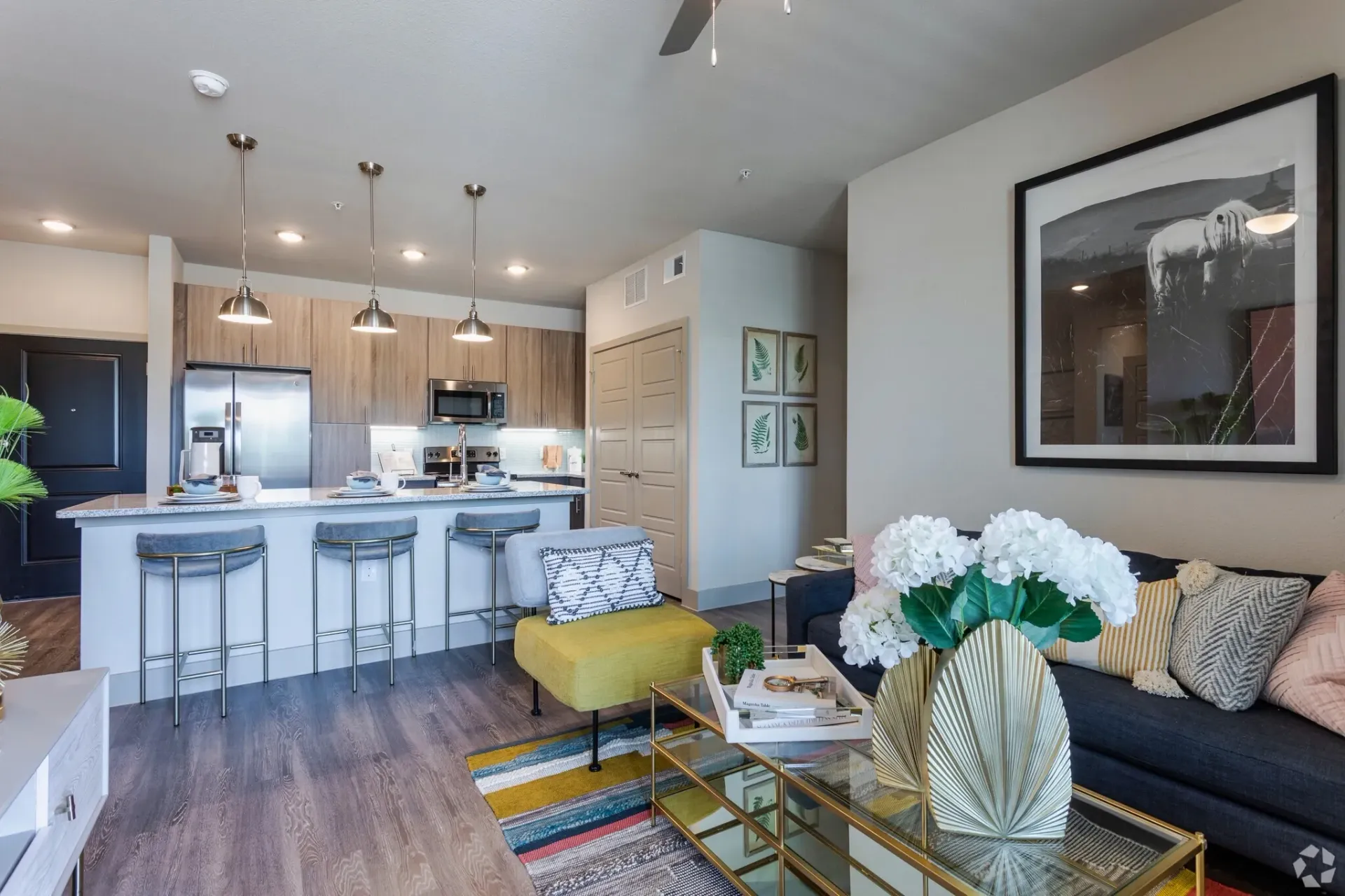 Open-concept living area with a kitchen island, bar stools, and a grey sofa in a modern apartment.