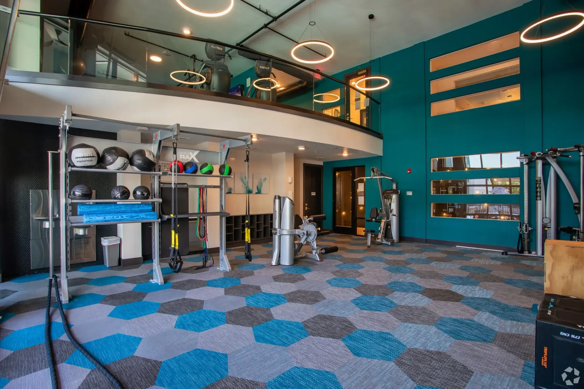 Interior of a community gym with teal walls, circular ceiling lights, and fitness equipment.