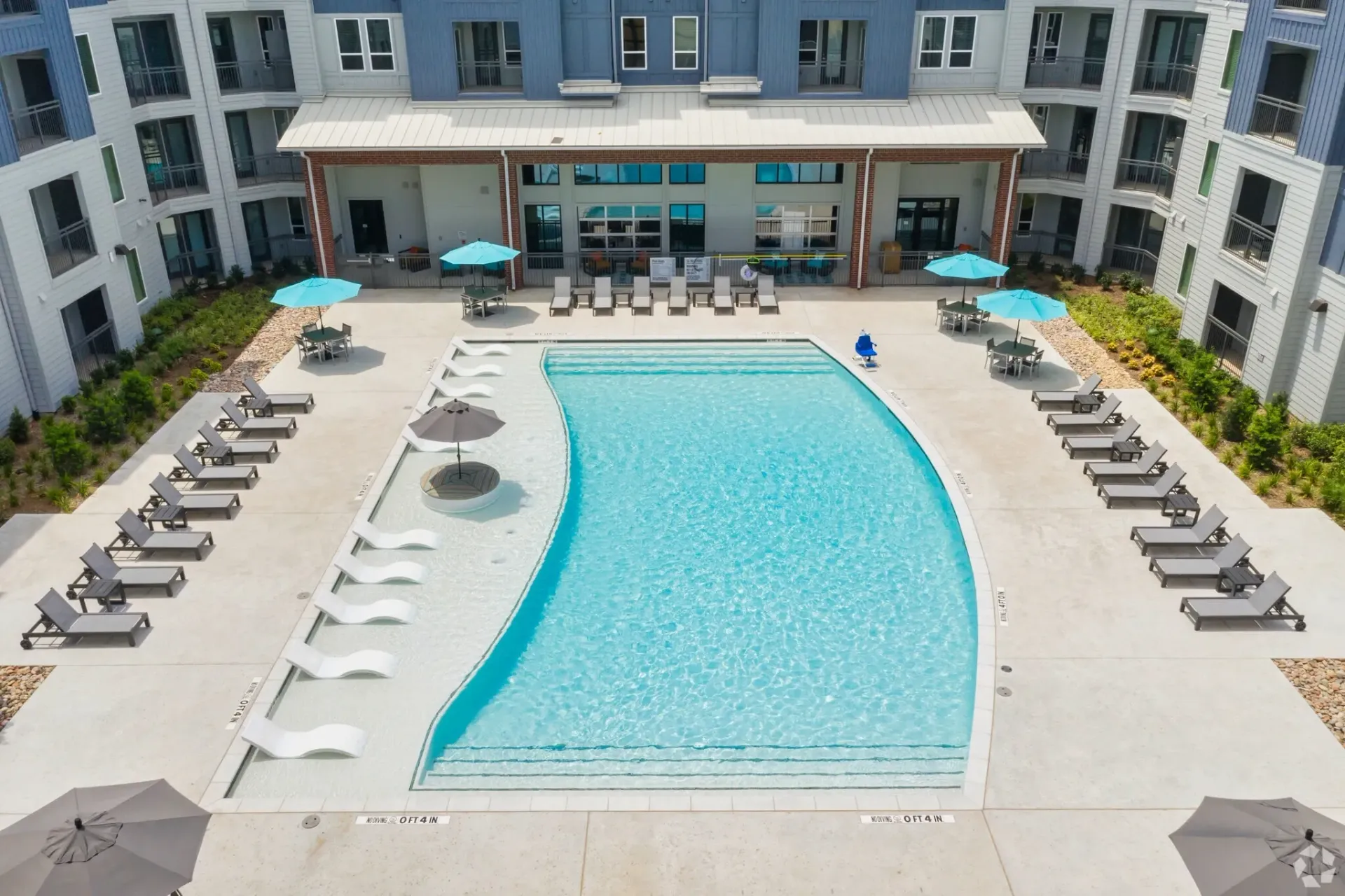 Aerial view of a communal outdoor pool in a modern apartment complex, with lounge chairs and blue umbrellas.