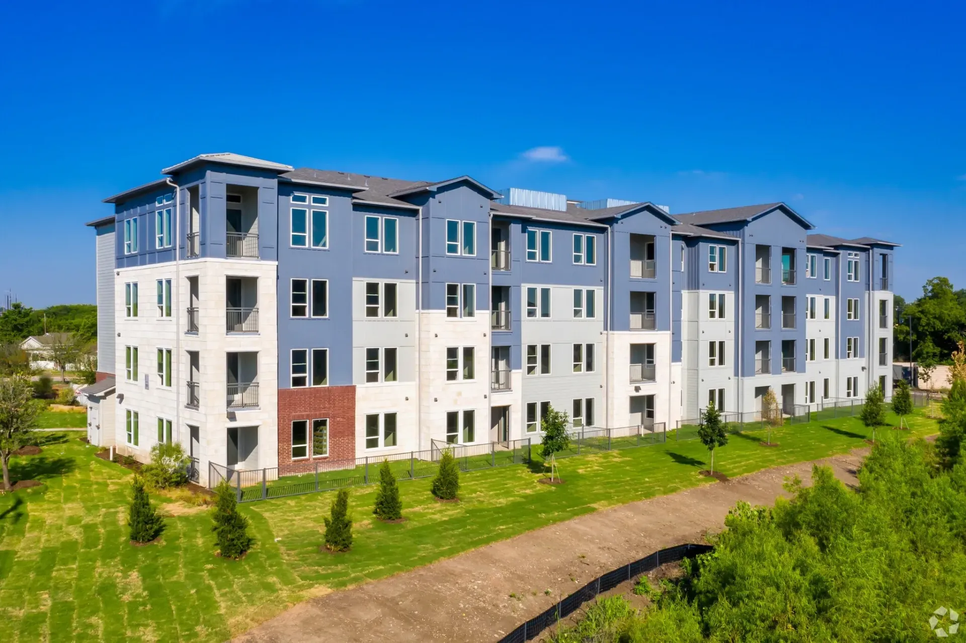 Exterior view of a modern apartment building with blue and white siding and a green lawn.