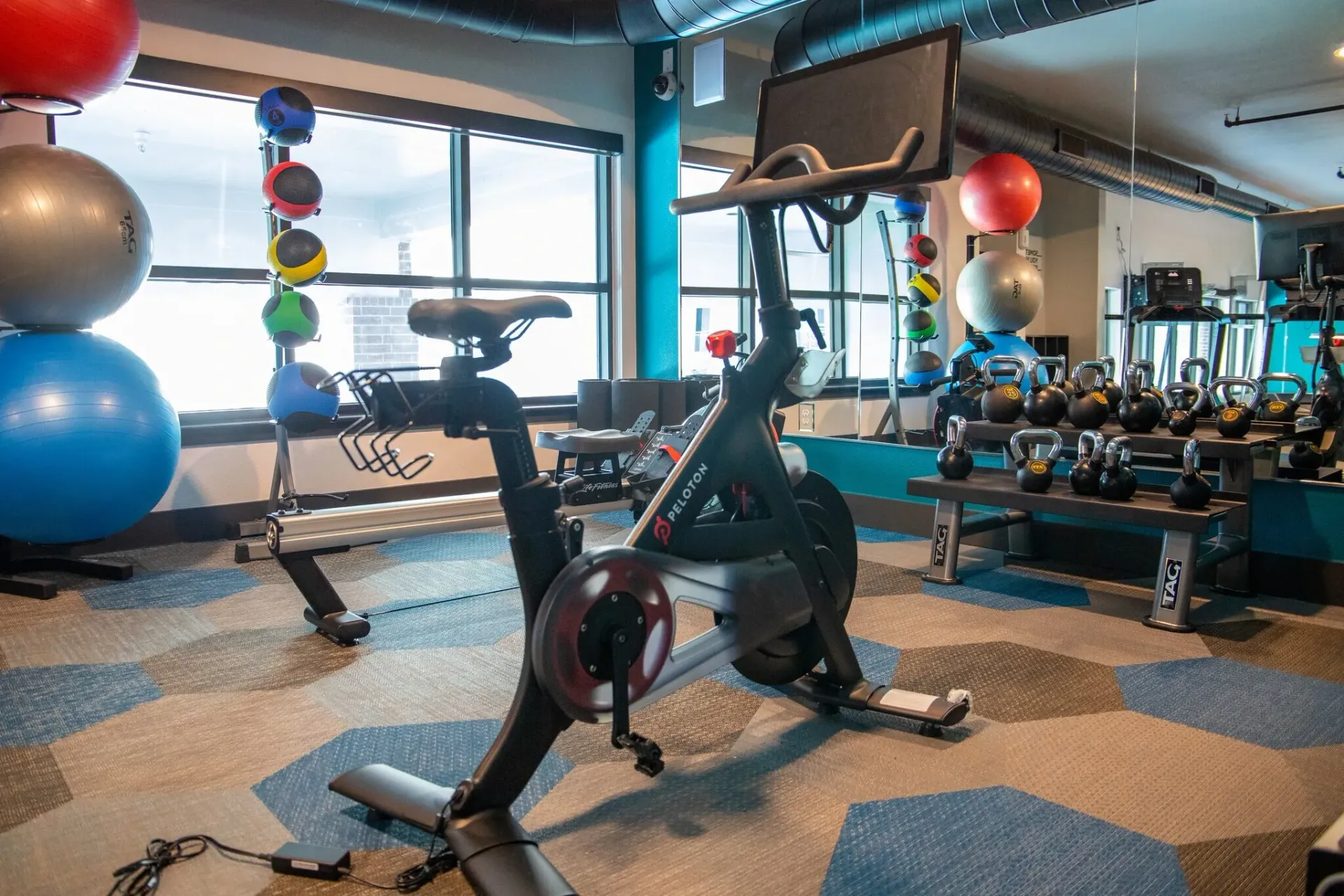 Indoor community gym with a stationary bike, kettlebells, medicine balls, and balance equipment.