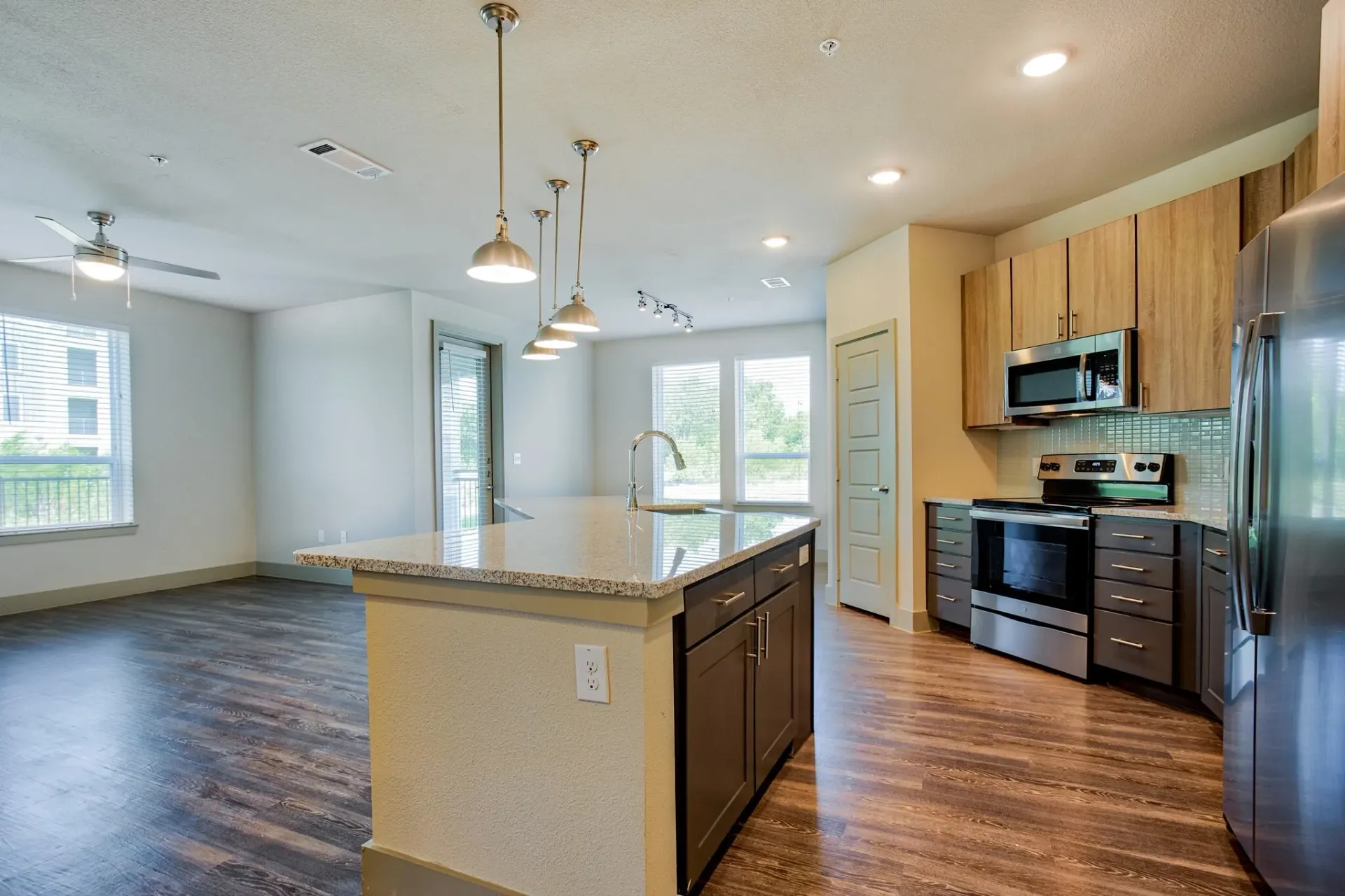 Open-concept kitchen with island, pendant lights, stainless steel appliances, and wood flooring.