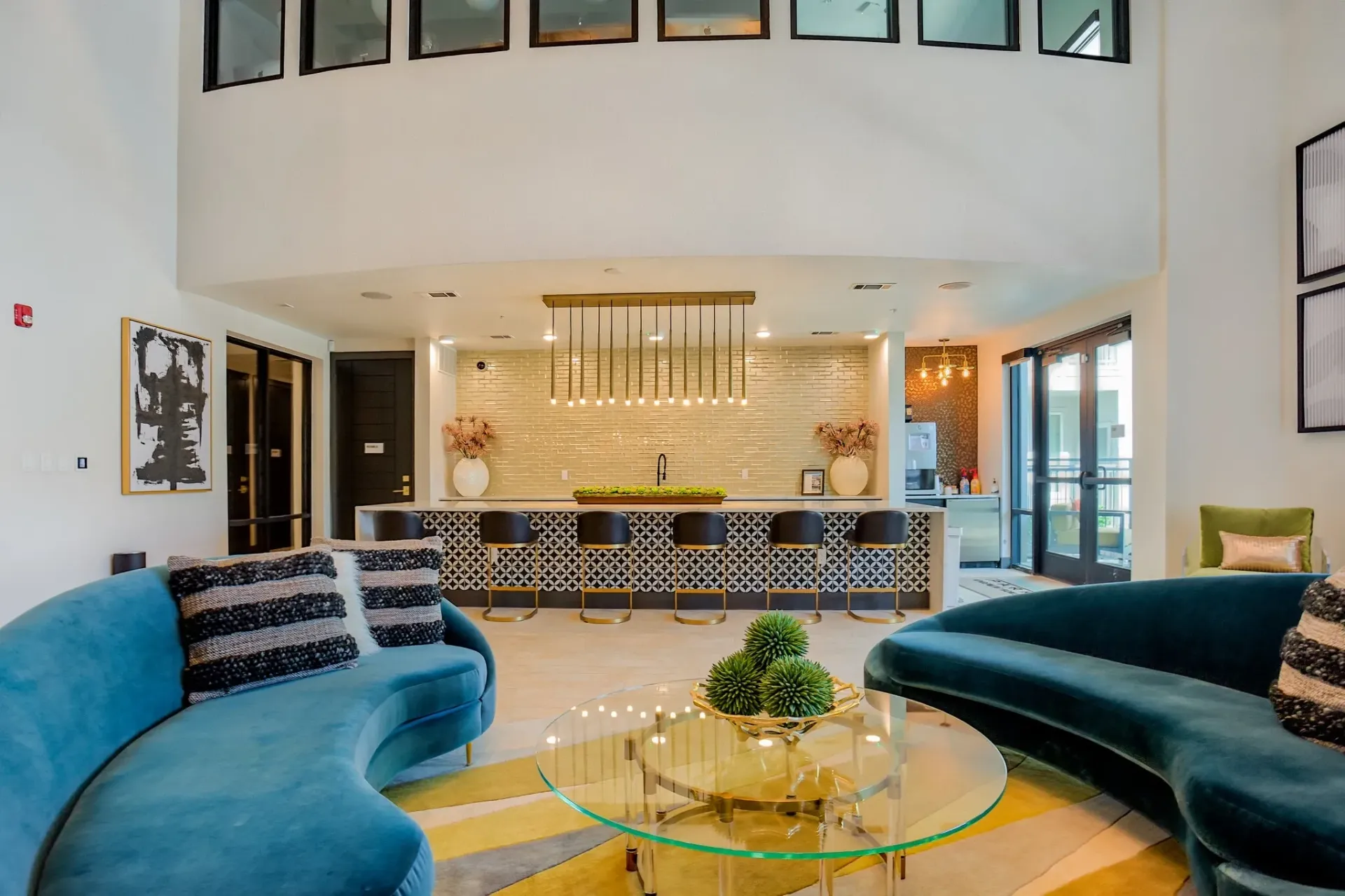 Modern resident lounge with curved teal sofas, glass coffee table, and a bar-height seating area.
