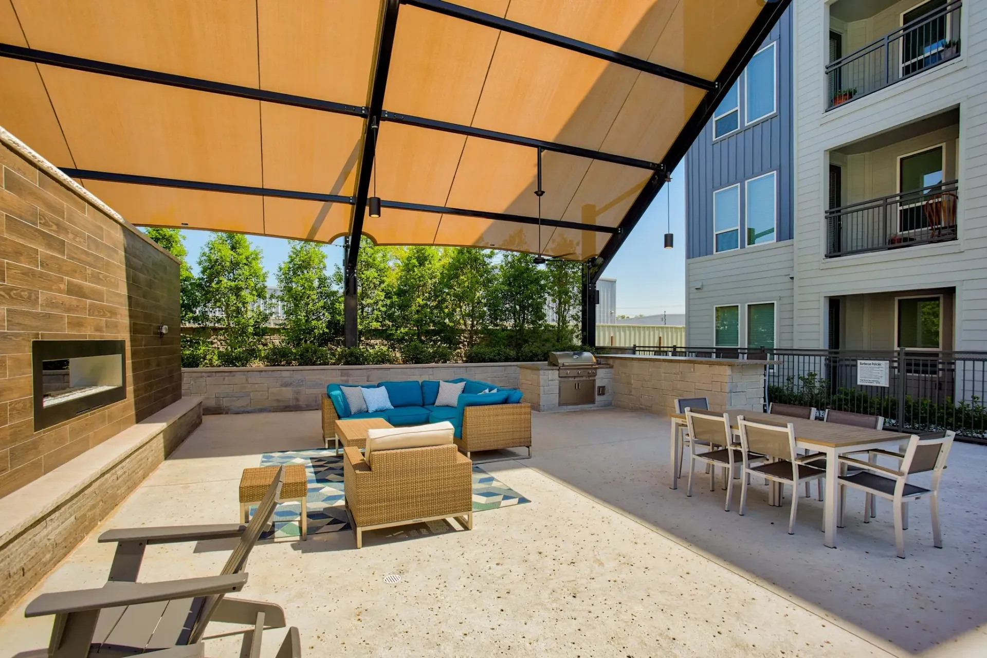Covered outdoor lounge area with wicker seating, a built-in grill, and a dining table.