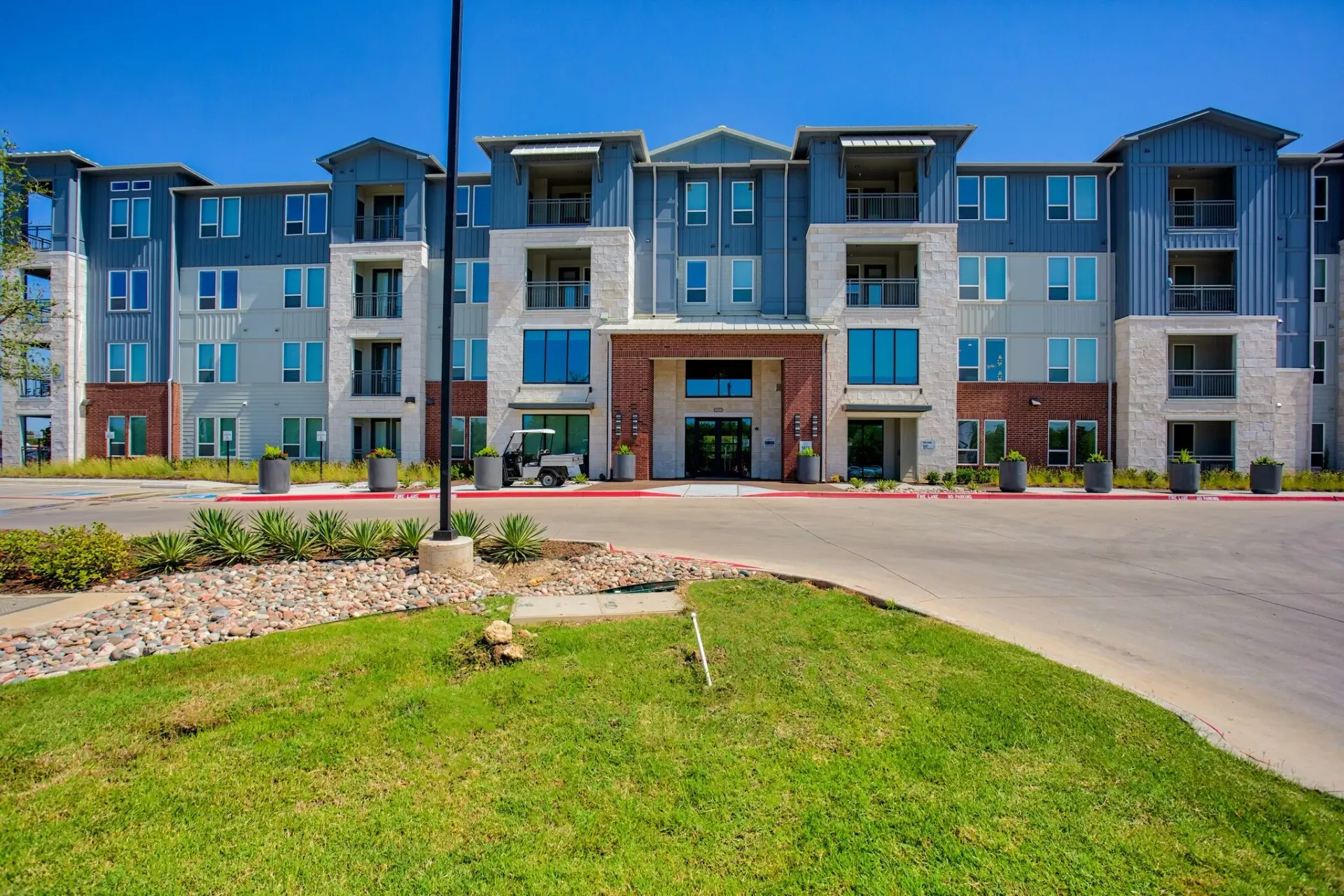 Exterior view of a modern apartment community building with landscaped entrance.
