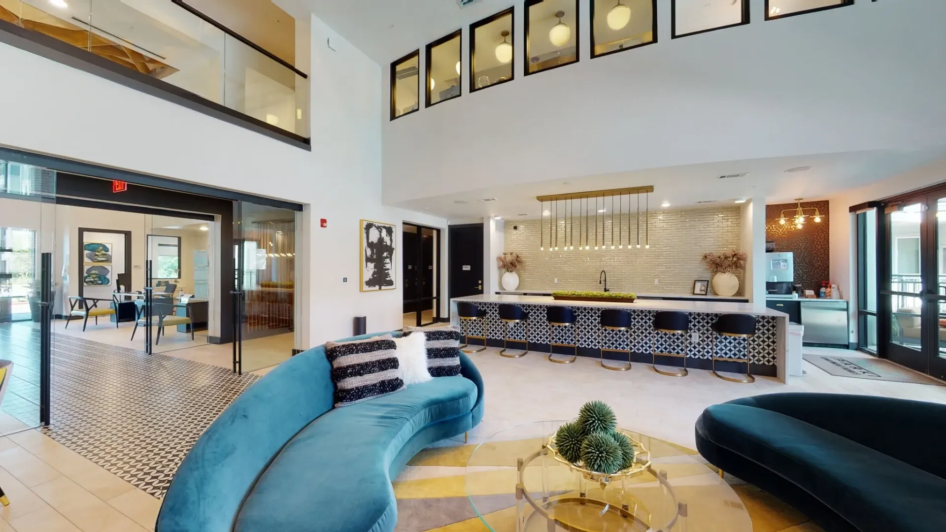 Bright open lobby with teal curved sofas, glass coffee table, and a bar area with stools.