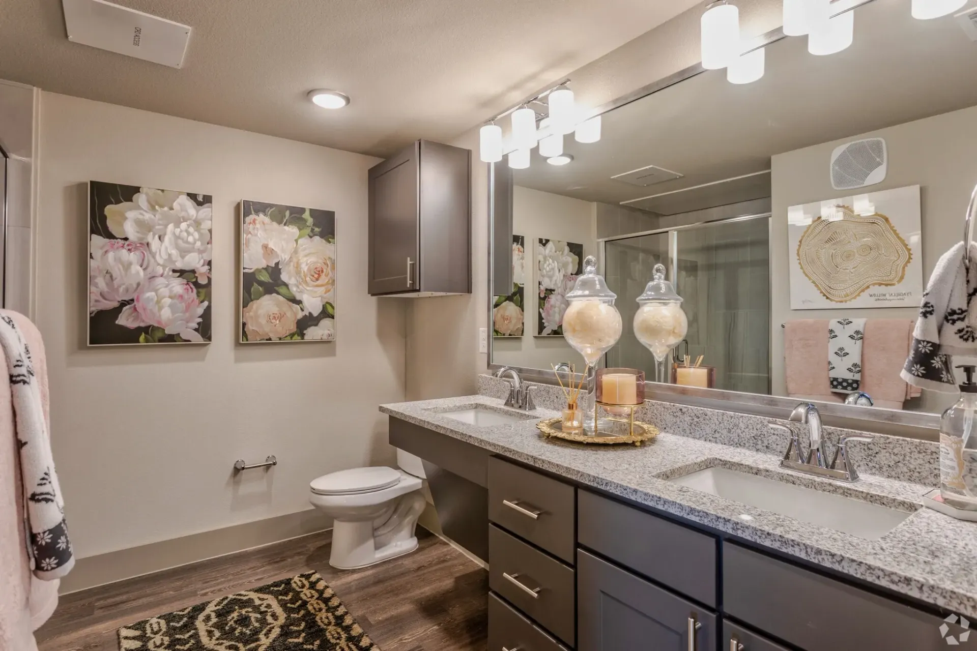 Modern apartment bathroom with dual sinks, granite countertop, and a large mirror.