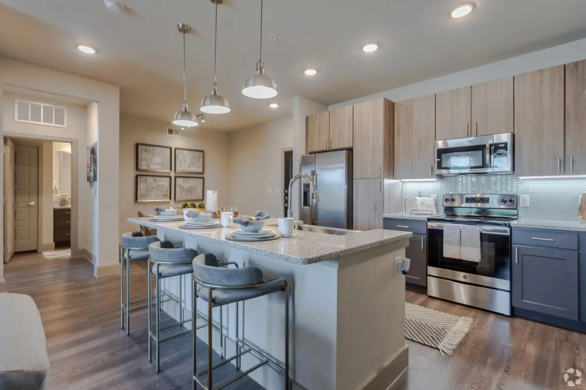 Open-concept modern apartment kitchen with island, pendant lights, and stainless-steel appliances.