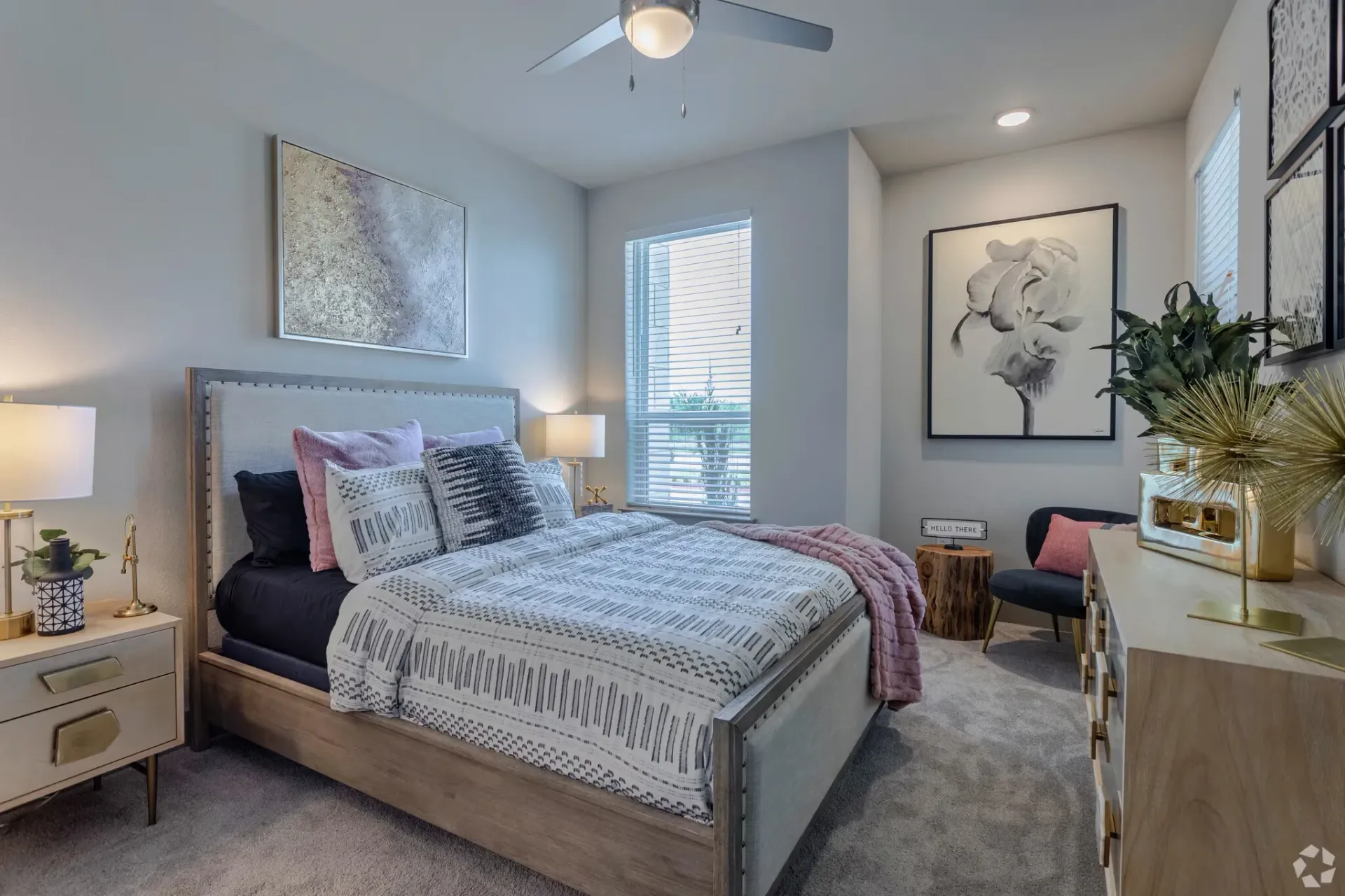 Bedroom in a modern apartment with an upholstered headboard, two nightstands, dresser, and framed art.
