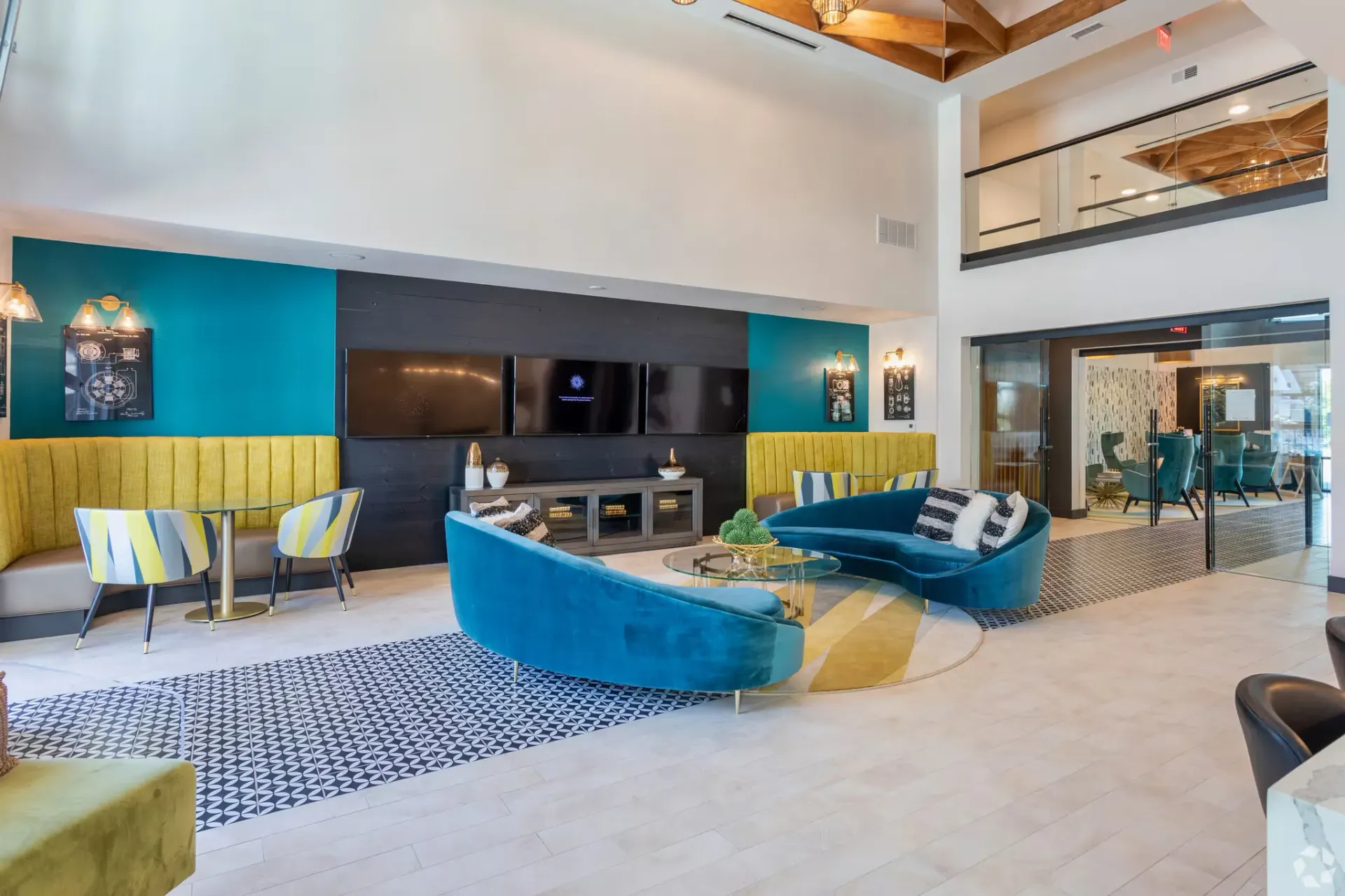 Bright apartment lobby with teal accent wall, yellow banquettes, curved blue sofas, and glass-walled meeting room.