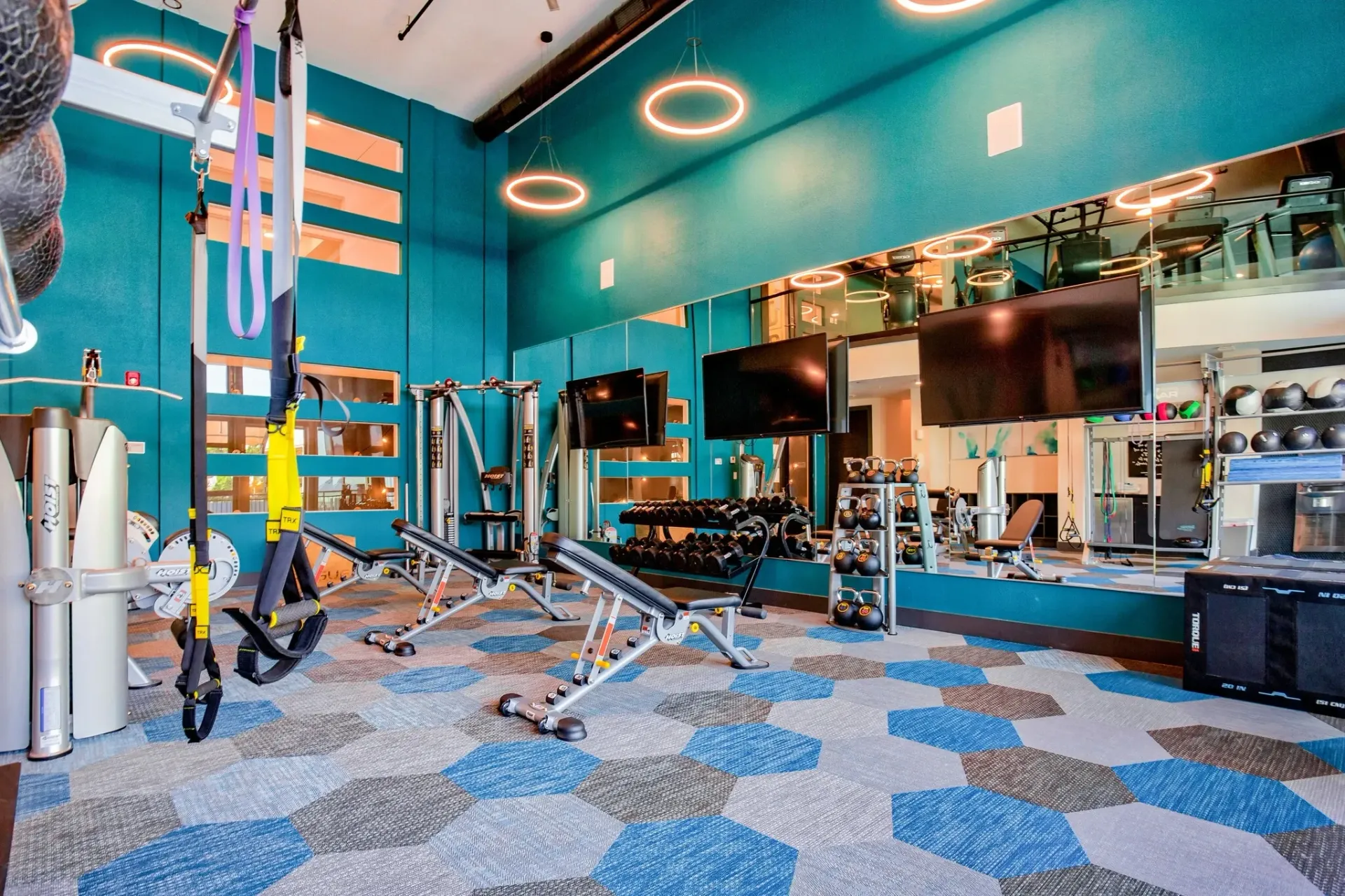 Indoor fitness center with teal walls, cardio machines, free weights, and large mirrors.