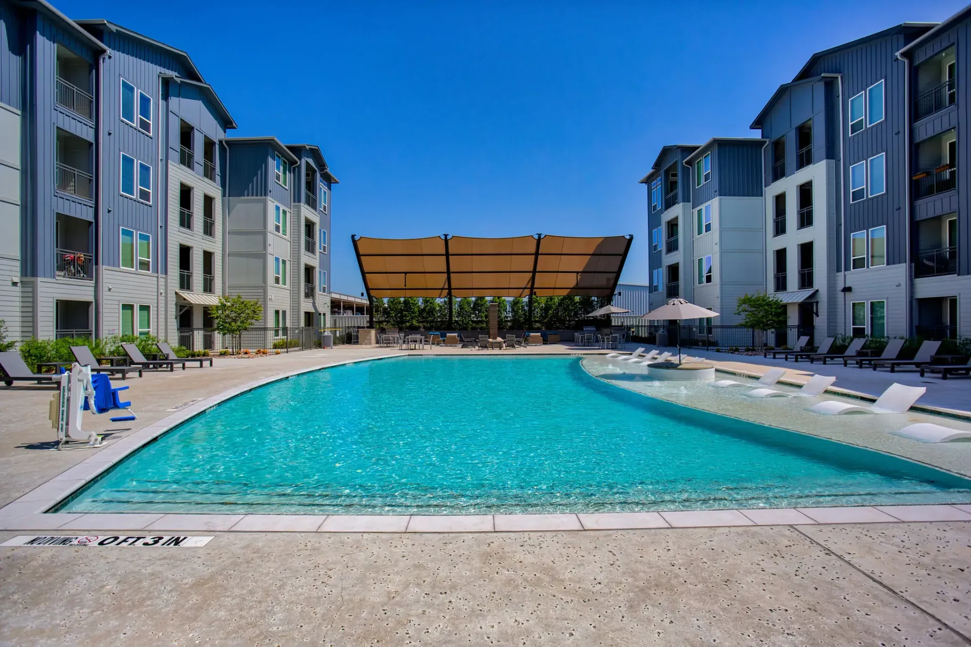 Outdoor pool at an apartment community, surrounded by lounge chairs and shade structures.