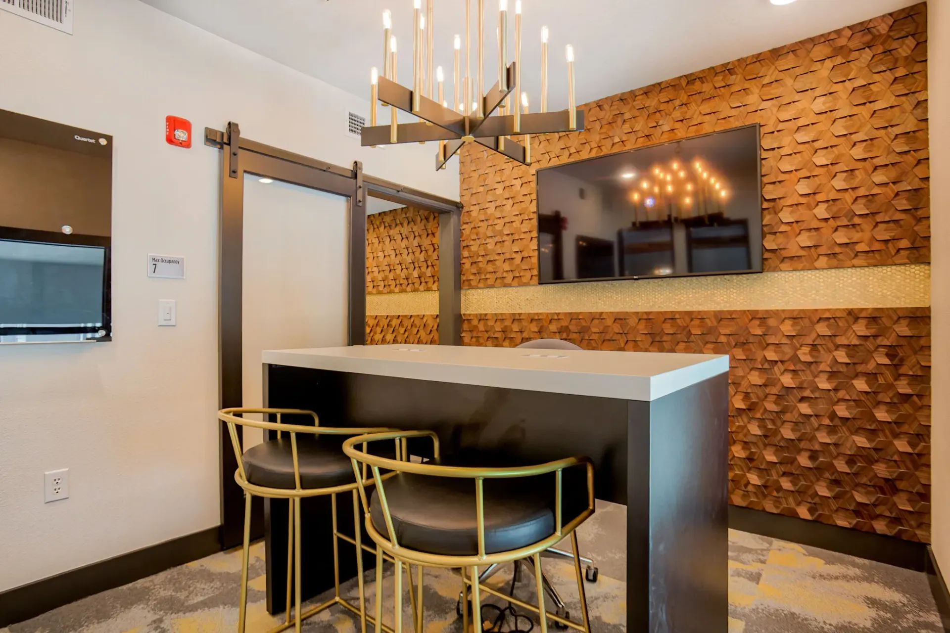 Modern community lounge with a high table, gold chairs, and a textured wood wall.