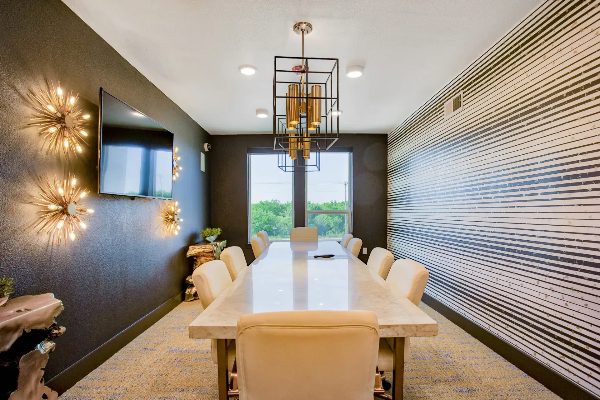 Conference room with a long marble table, beige chairs, dark accent wall, and modern lighting.