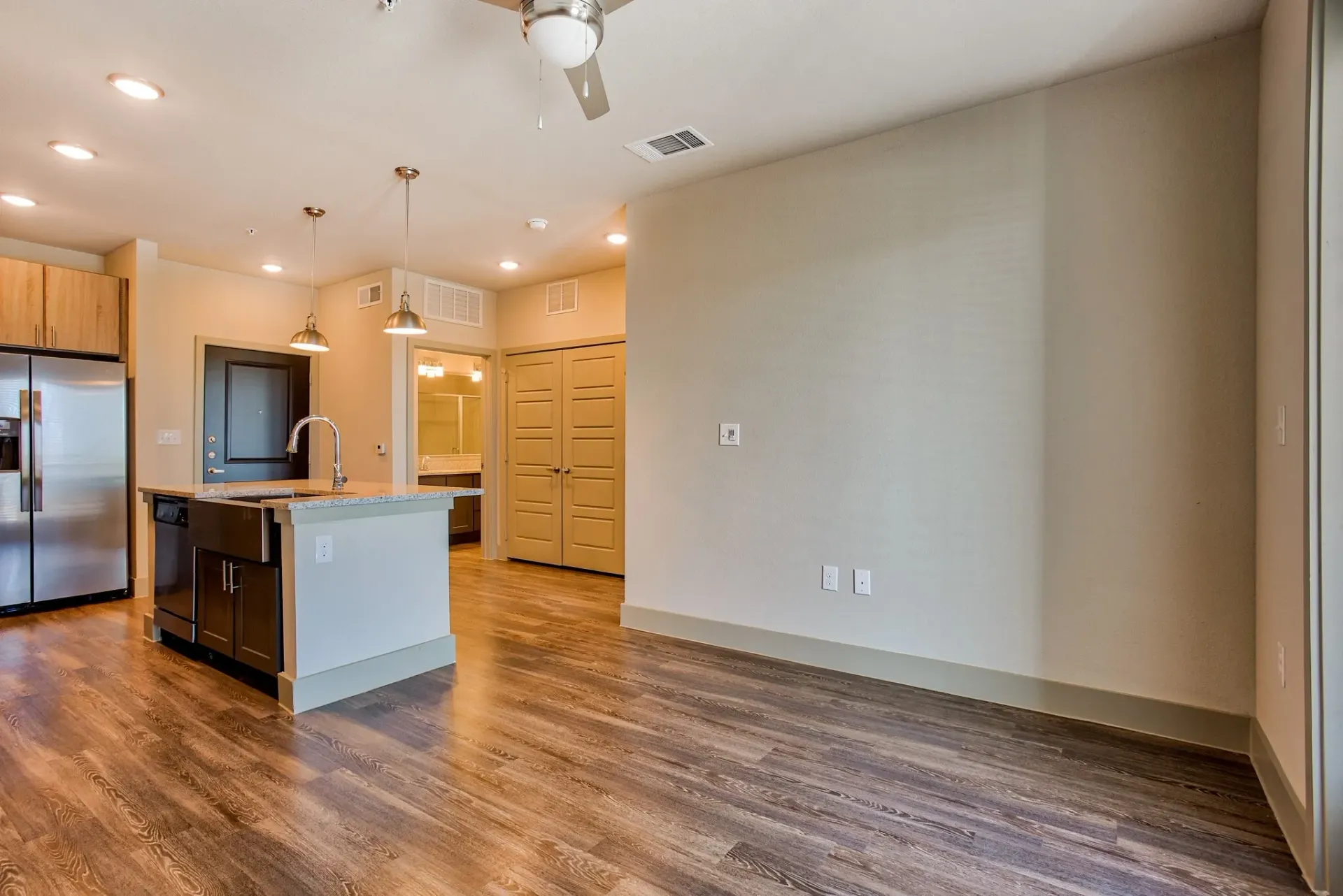 Open-concept kitchen with island, pendant lights, and stainless steel appliances in a modern apartment.