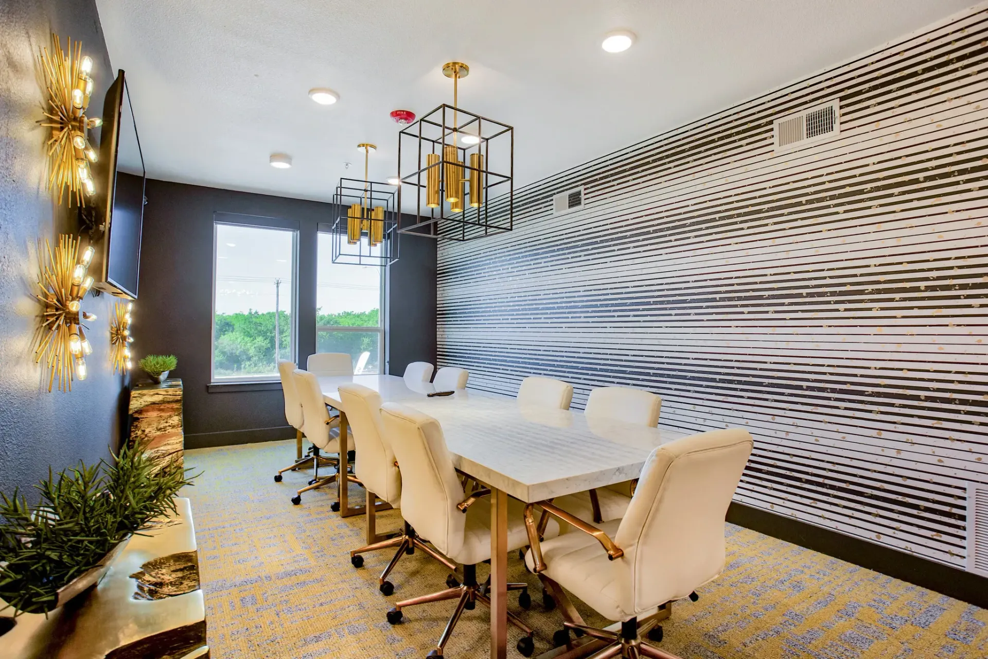 Modern community conference room with a long white marble table, cream chairs, and a striped accent wall.