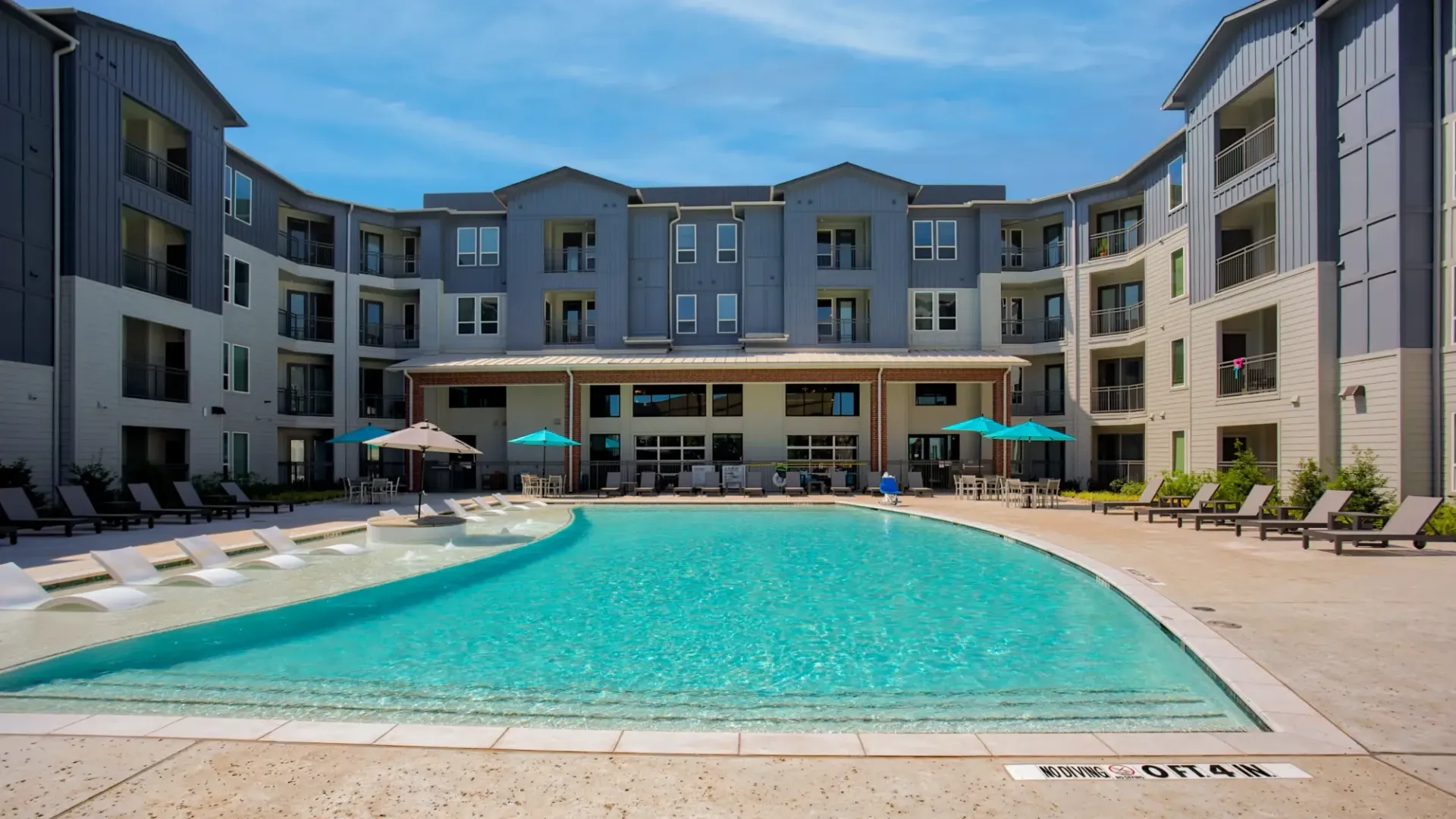 Outdoor pool at a modern apartment community with lounge chairs and umbrellas.