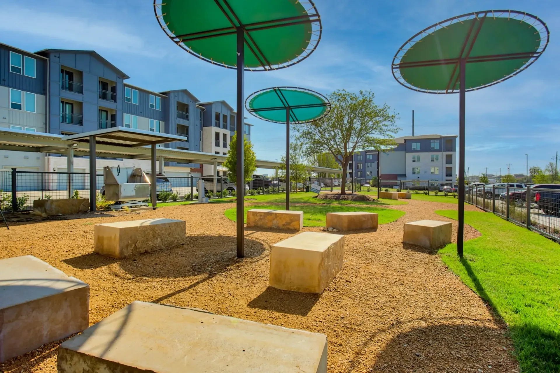 Outdoor community courtyard with circular green shade canopies, concrete benches, and apartment buildings in the background.