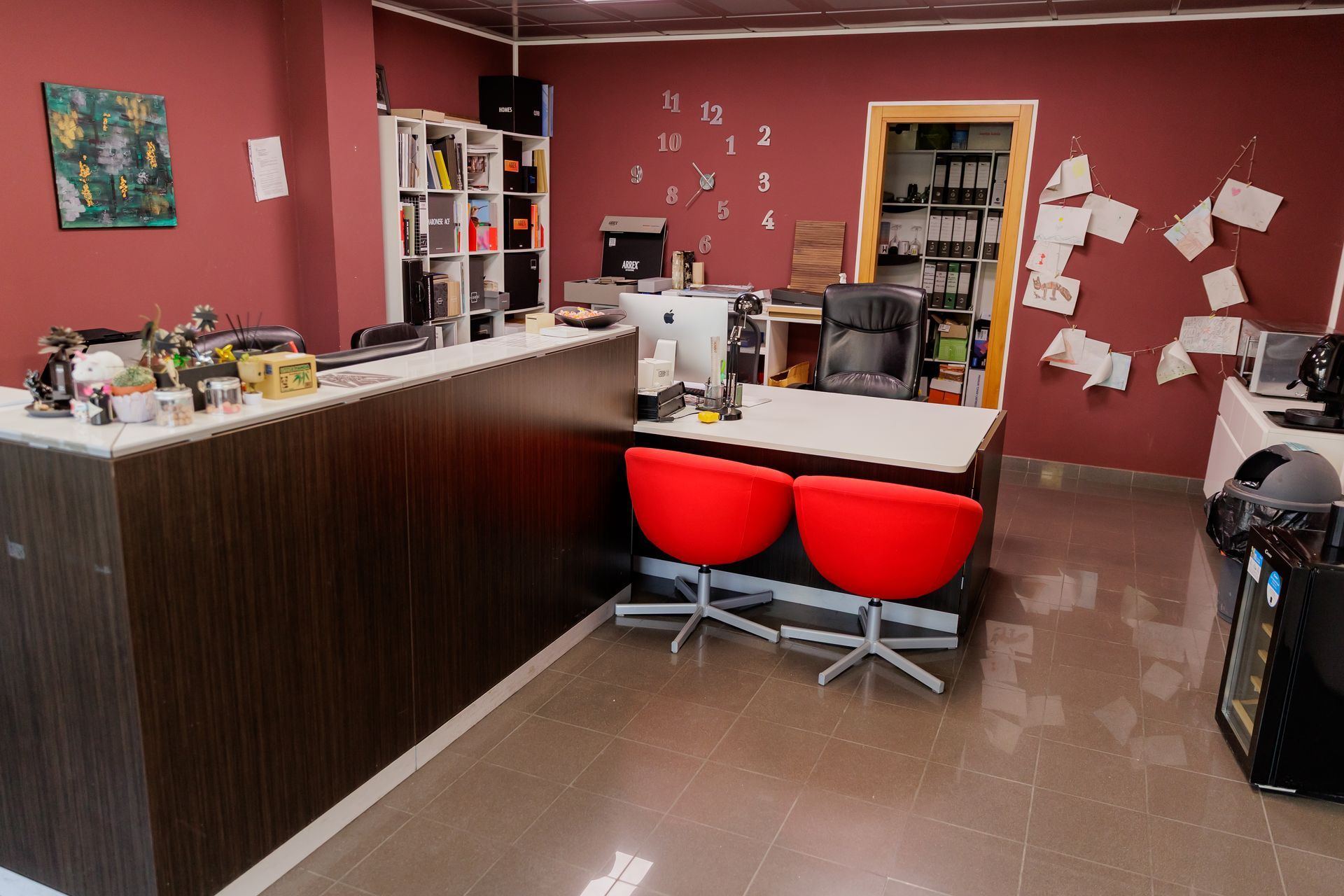 Una reception professionale con scrivania in legno scuro, pavimento in piastrelle grigie lucide e pareti color bordeaux sotto un soffitto metallico.