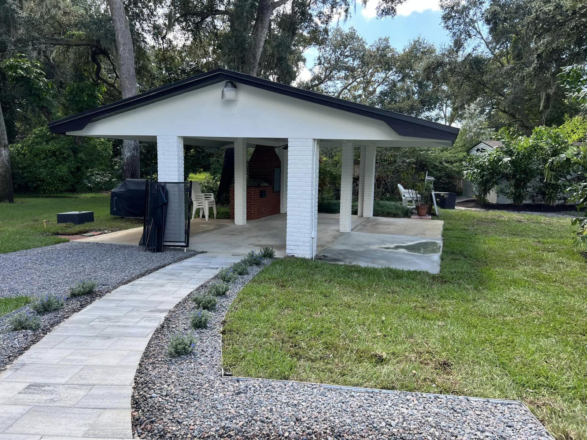 A covered outdoor patio with a stone pathway and a grassy lawn.