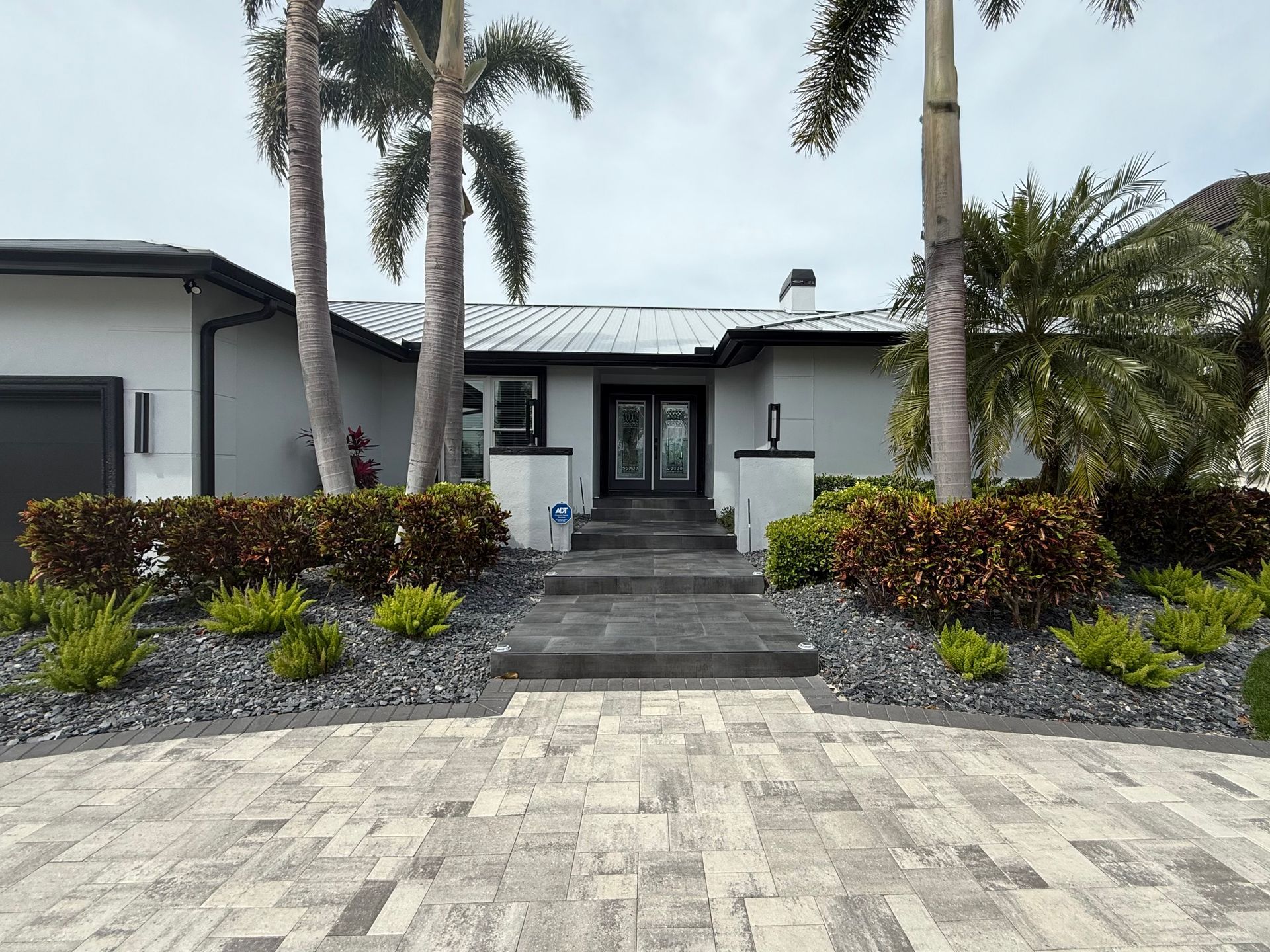 A modern house with a stone driveway, landscaping, and palm trees.