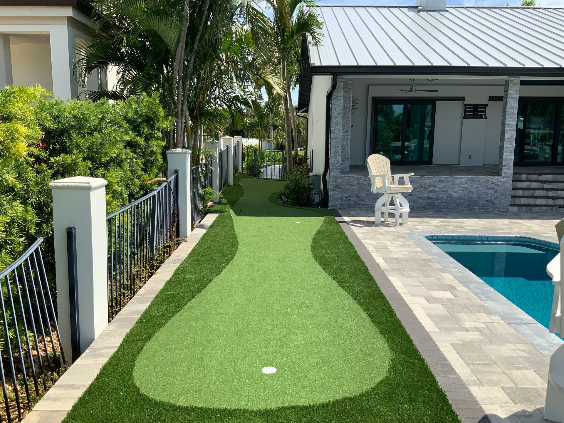 A house with a swimming pool and a putting green in front of it.