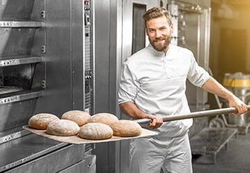 Baker Taking Out From the Oven Baked Bread — Restaurant Equipment & Supplies in Daytona Beach, FL