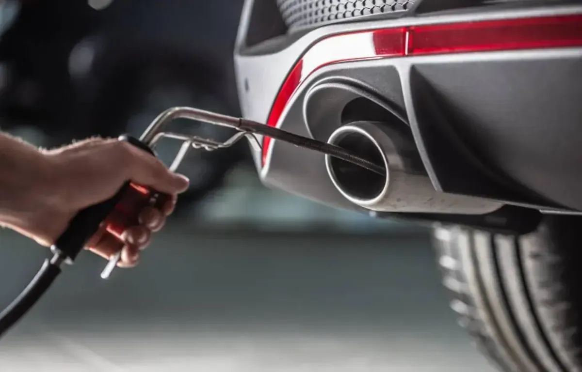 A person tests a car's exhaust emissions with a probe in a close-up shot.