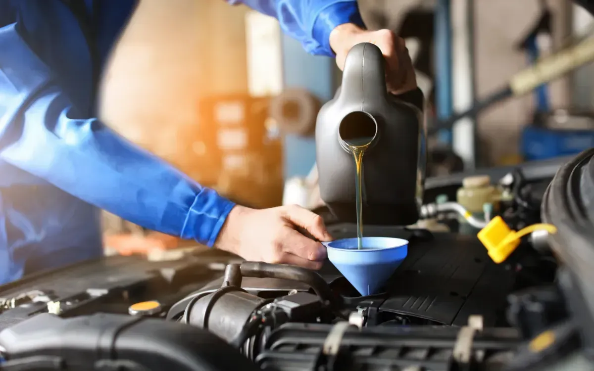 Mechanic pouring oil into a car engine, wearing gloves.