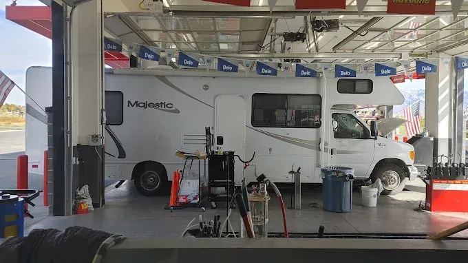 RV in a service bay with the hood open. Tools and a person are present.