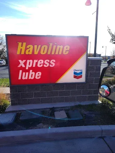 Havoline Xpress Lube sign with red and yellow text, chevron logo, brick base, daytime.