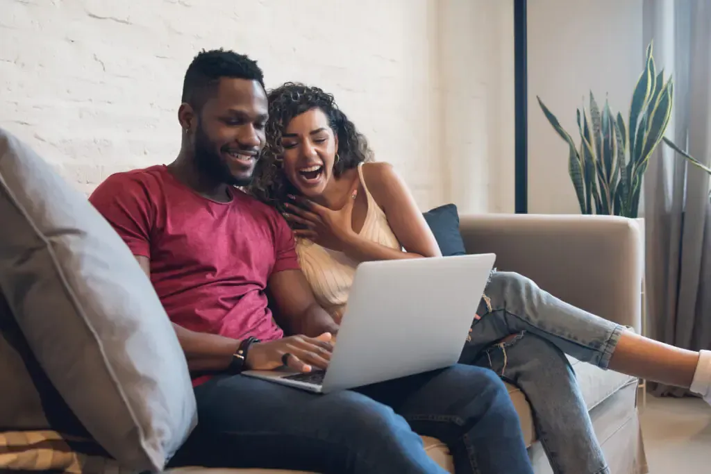 Couple laughing while looking at a laptop together on a couch.